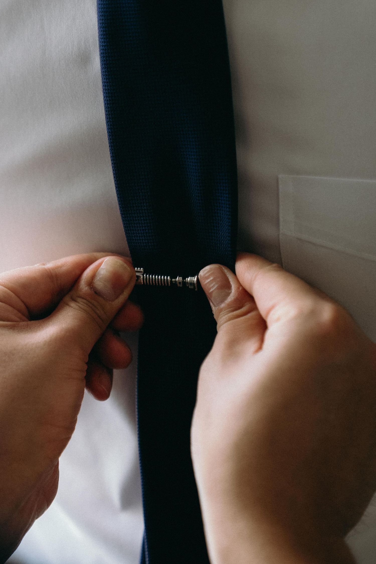 Close-up shots of hands adjusting a dark necktie against a light background.