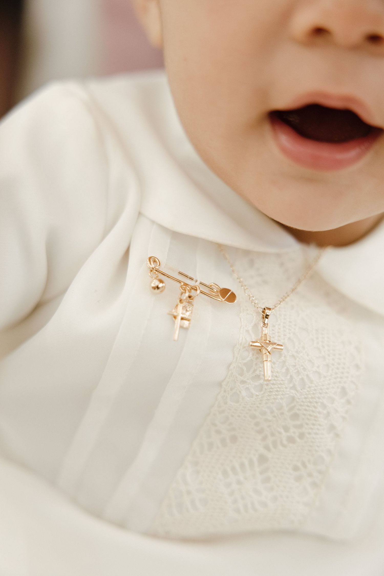 Close-up of delicate gold cross pins on white baptismal garment.