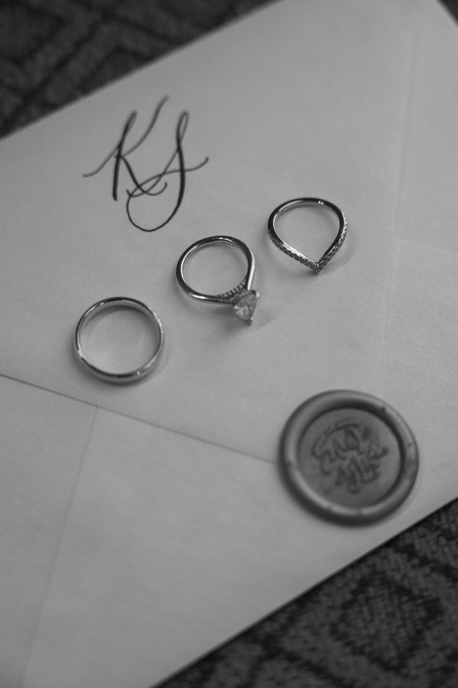 Wedding rings and wax seal displayed on white paper in black and white photography.