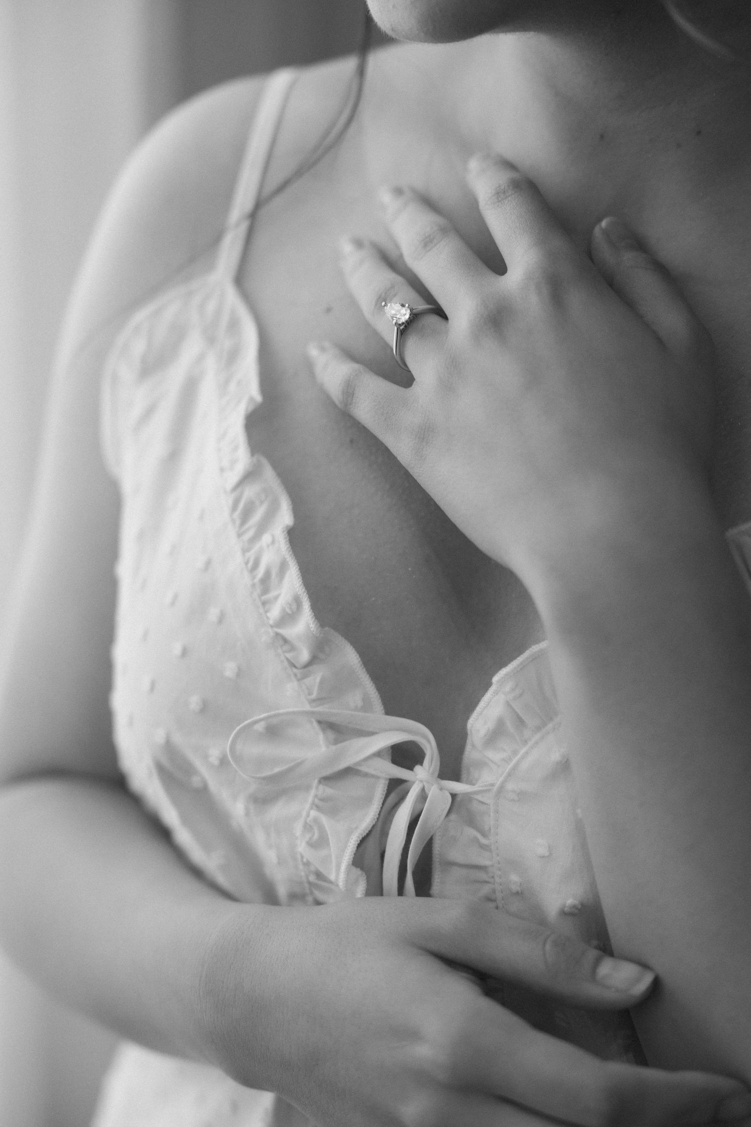 Close-up of an engagement ring on a bride's hand against white lace fabric.