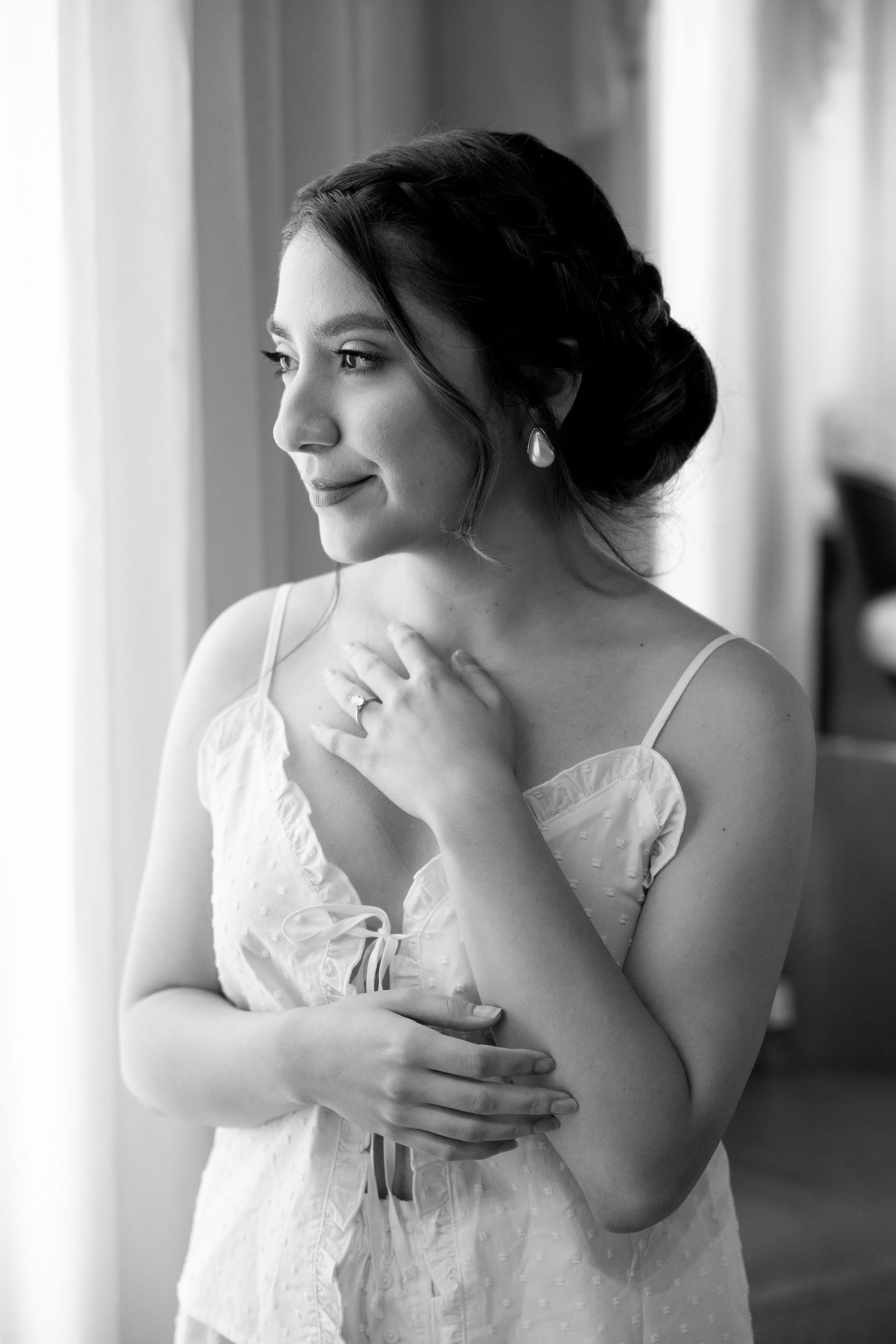 A bride in white lace poses by a window in an elegant black and white portrait.