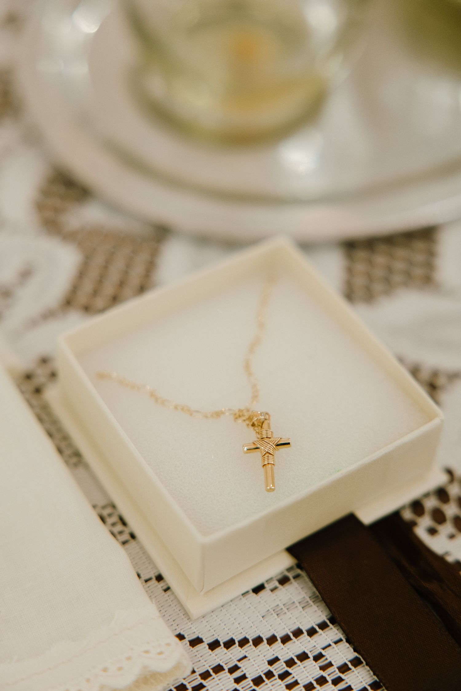 Gold cross necklaces displayed in white gift boxes on lace tablecloth.