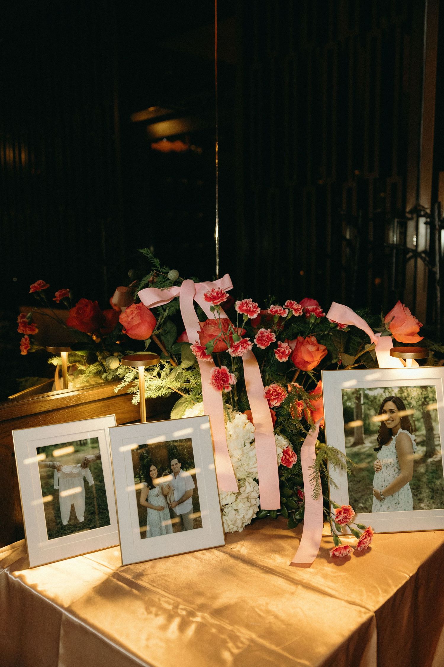 Framed photographs displayed with pink roses and ribbons in an elegant event setup.