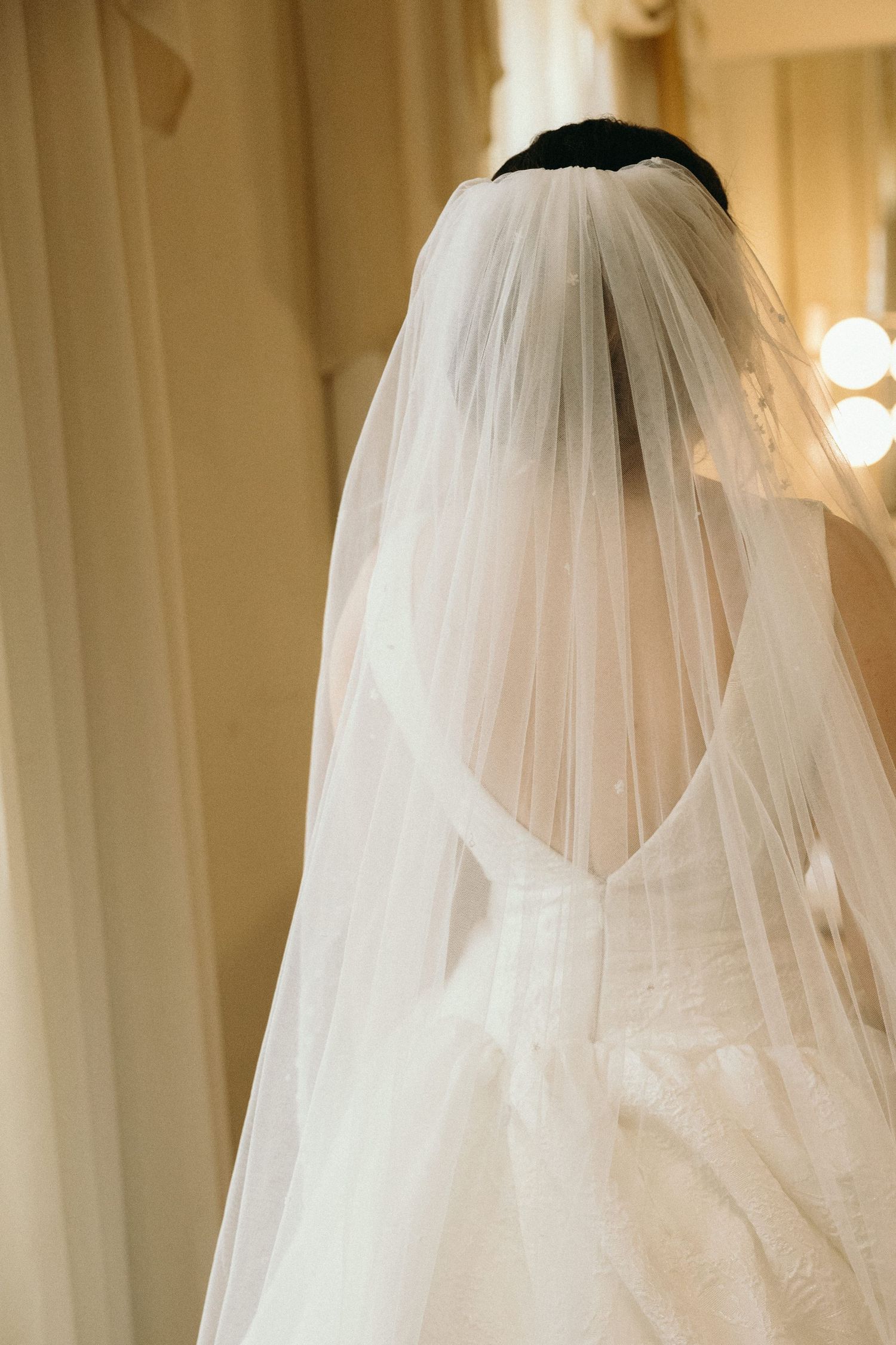 Delicate white wedding veil flowing in soft light against a warm beige background.