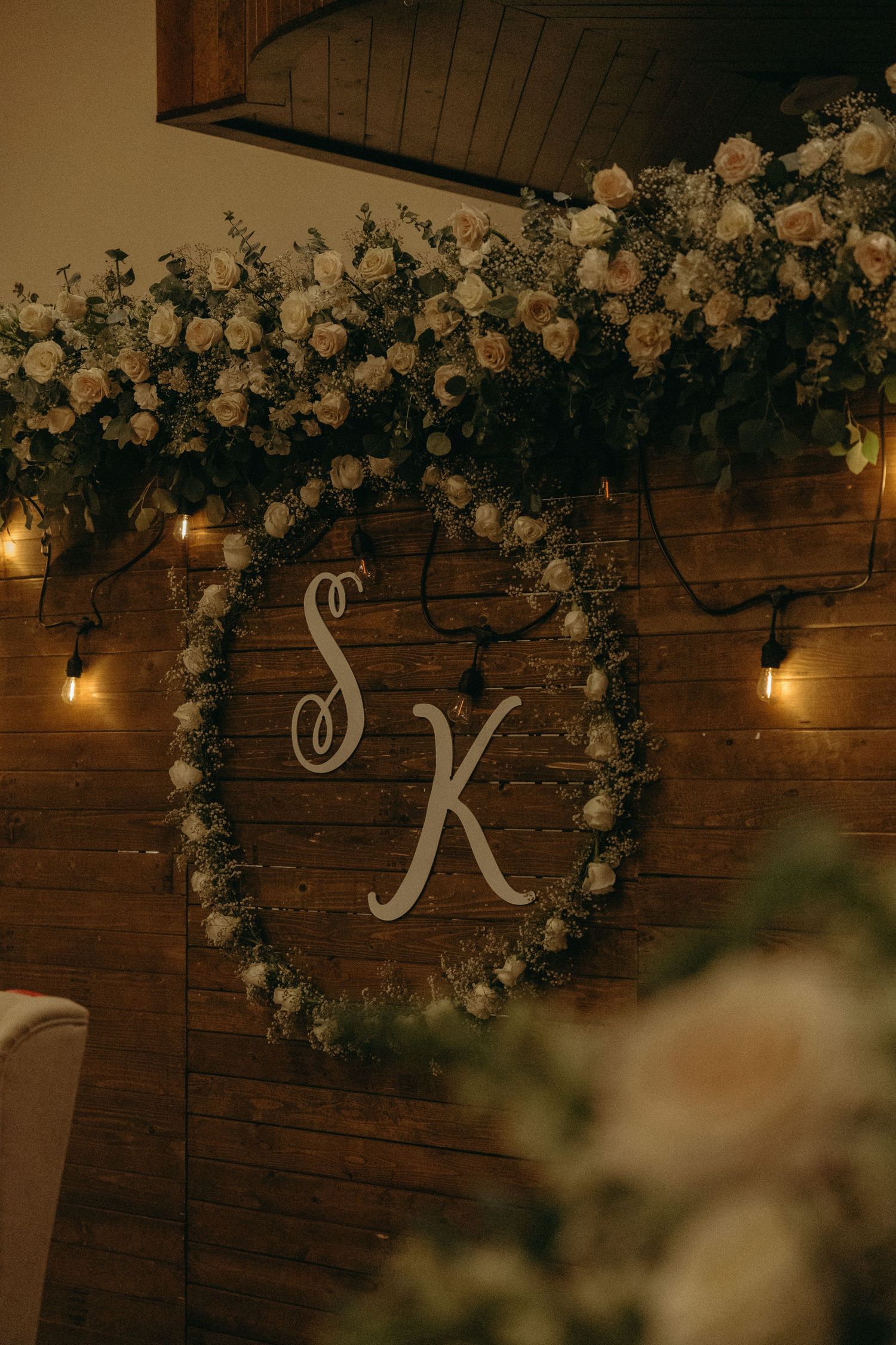 Rustic wooden wall decorated with white flowers and string lights for a wedding reception.