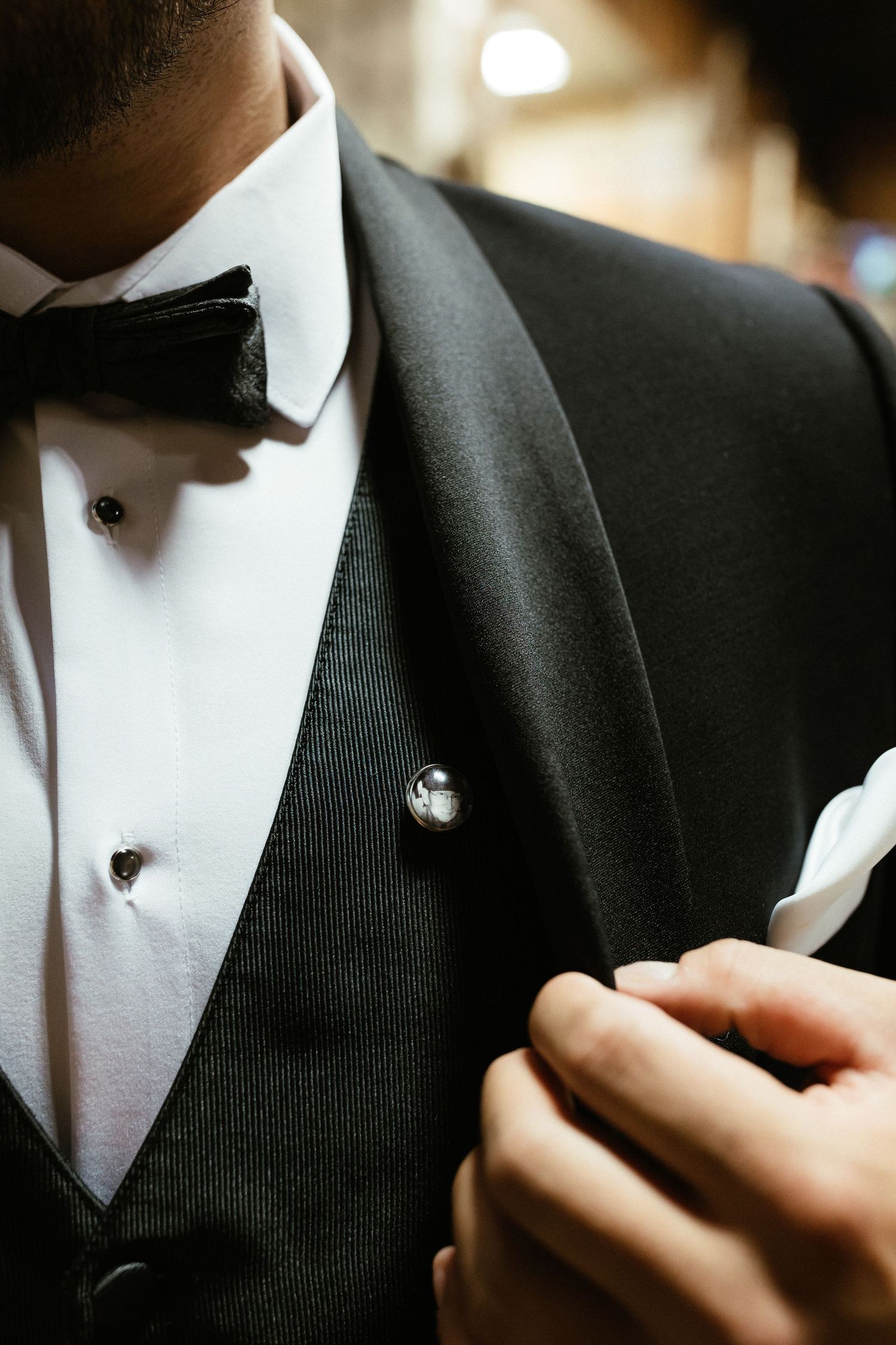 Close-up detail of formal black suit jacket and white dress shirt being adjusted.