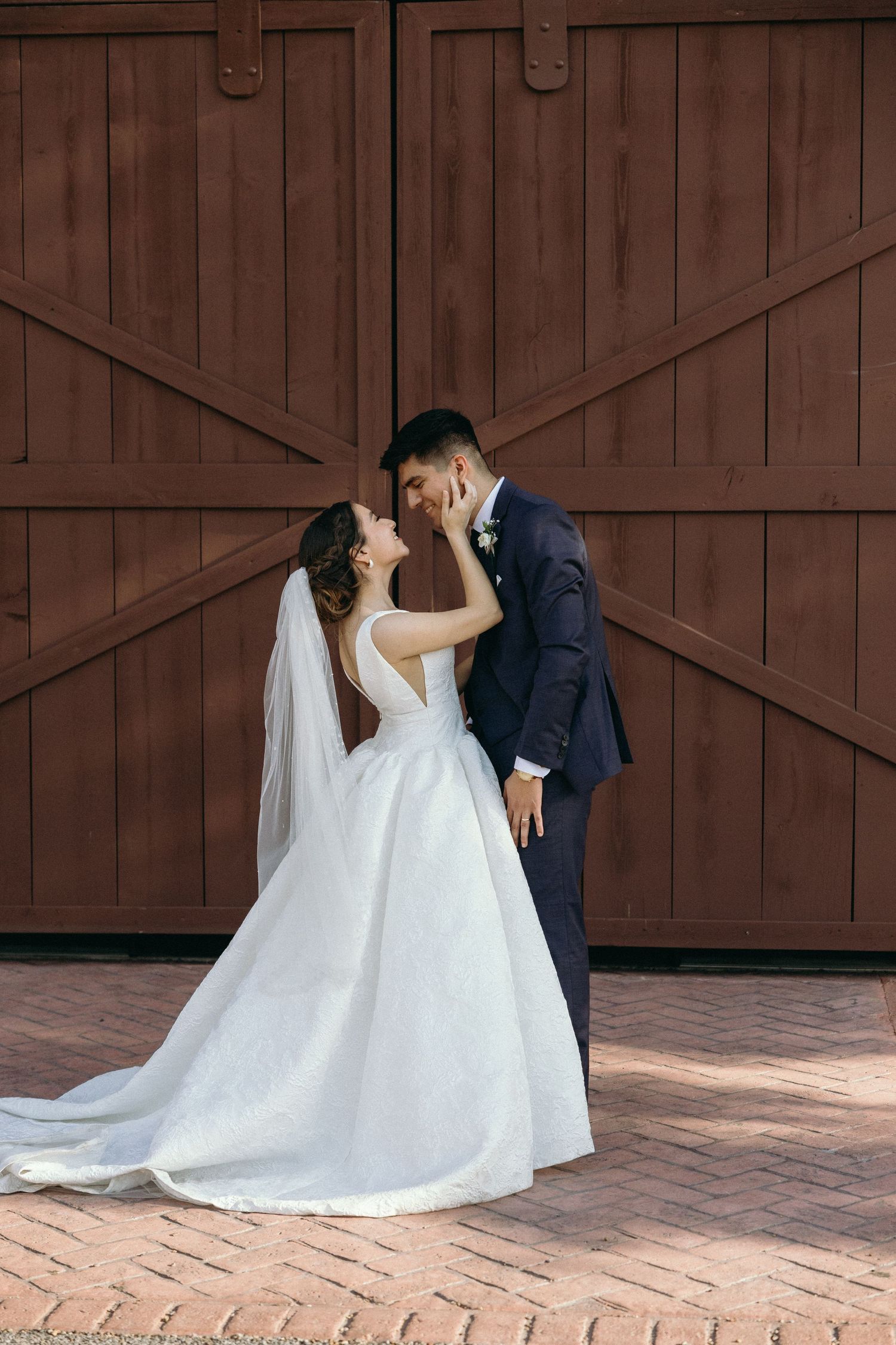 Wedding couple poses against rustic wooden barn doors.