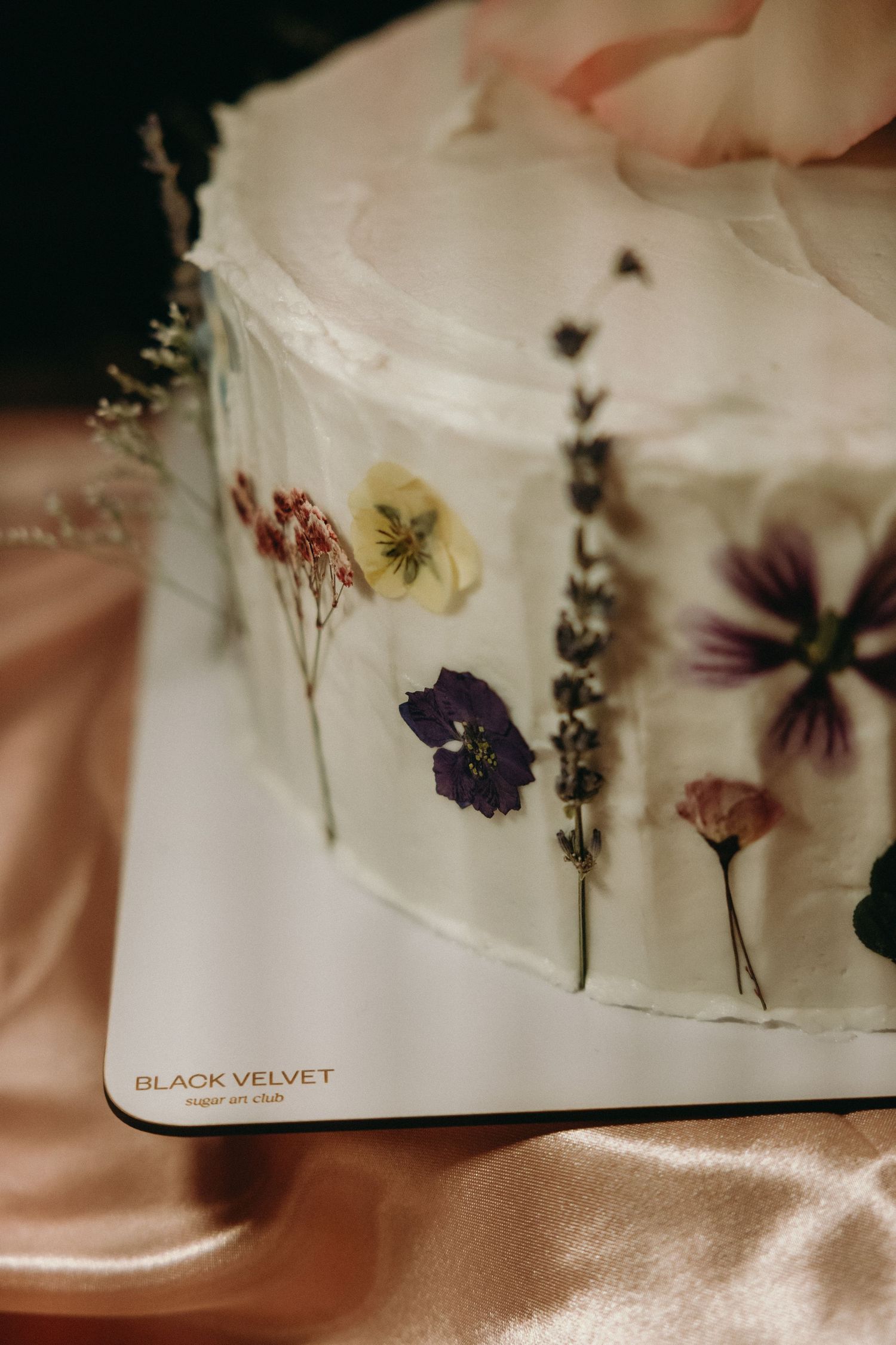 Close-up of a white cake decorated with pressed dried flowers along its sides.