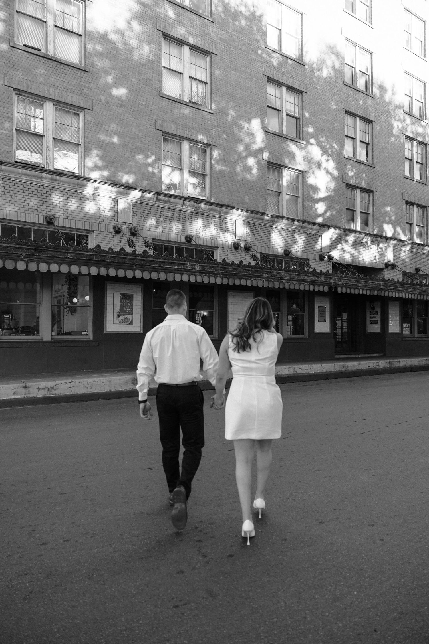 Black and white urban scene with figures walking past storefronts.