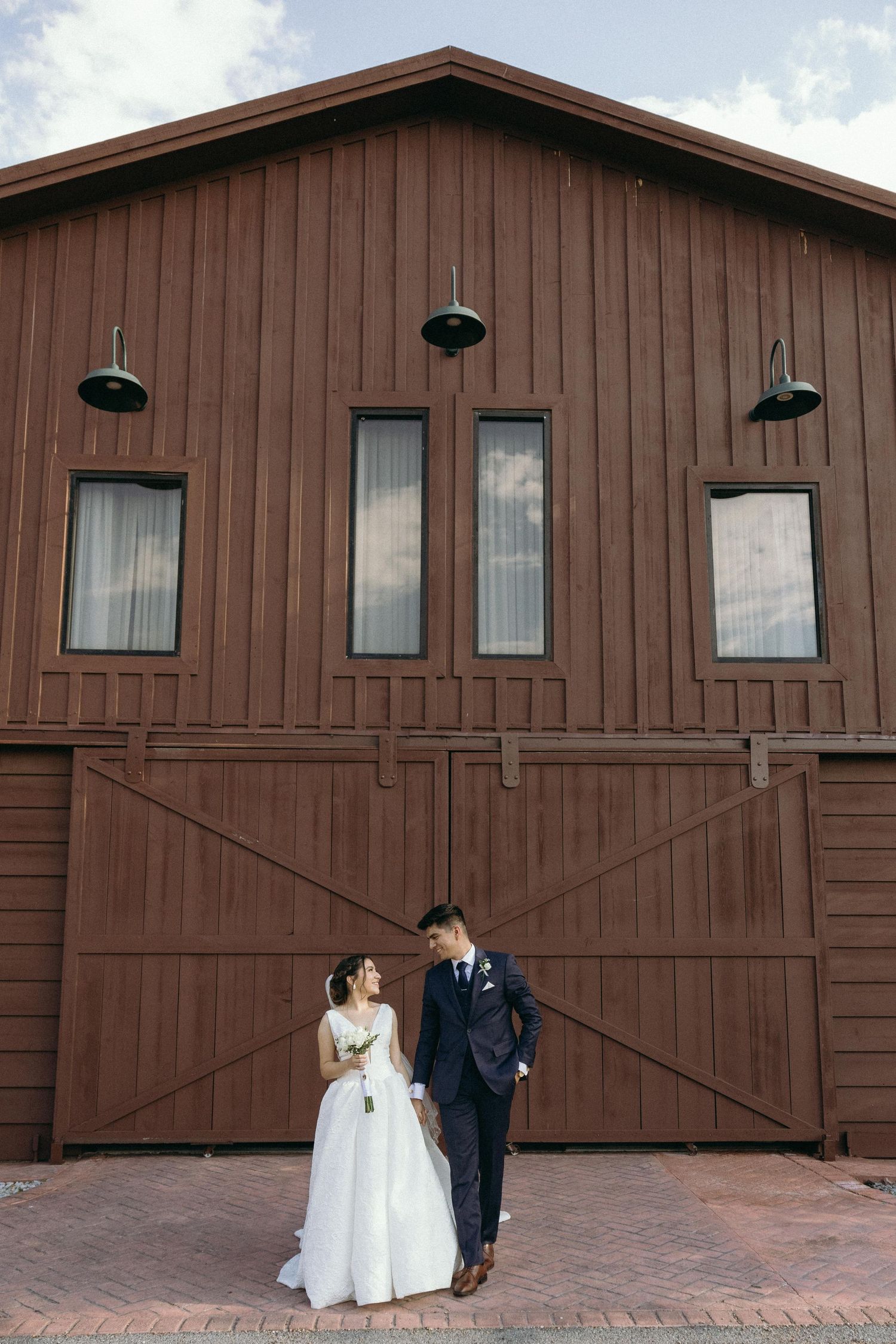 Wedding couple poses in front of rustic brown wooden building for photo sequence.
