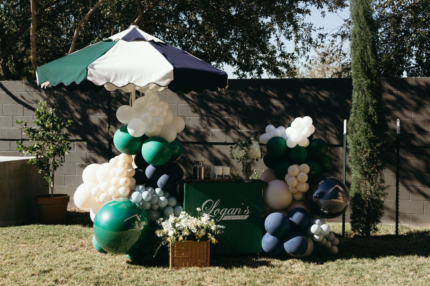 Outdoor party setup with green and white balloons arranged in an arch formation.