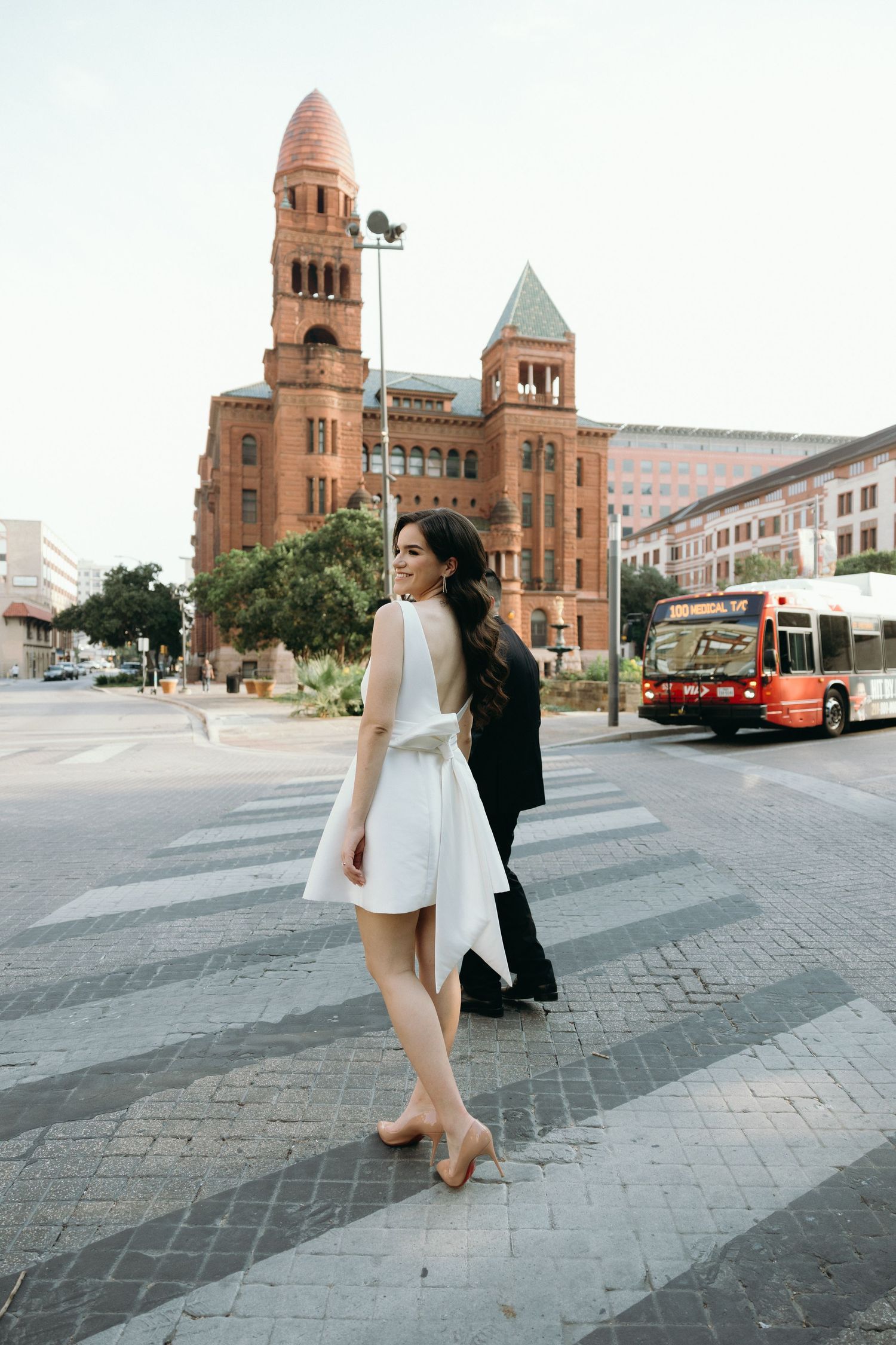 Couple walking on cobblestone plaza near historic red brick architecture.