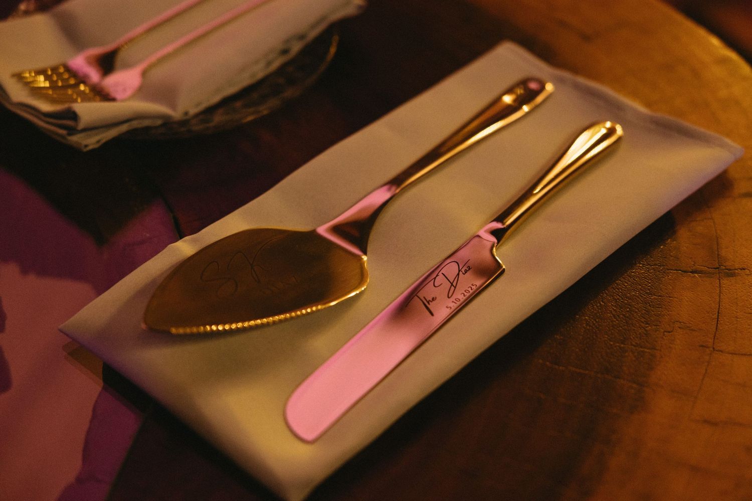 Place settings with gold utensils and pink accents on wooden table.