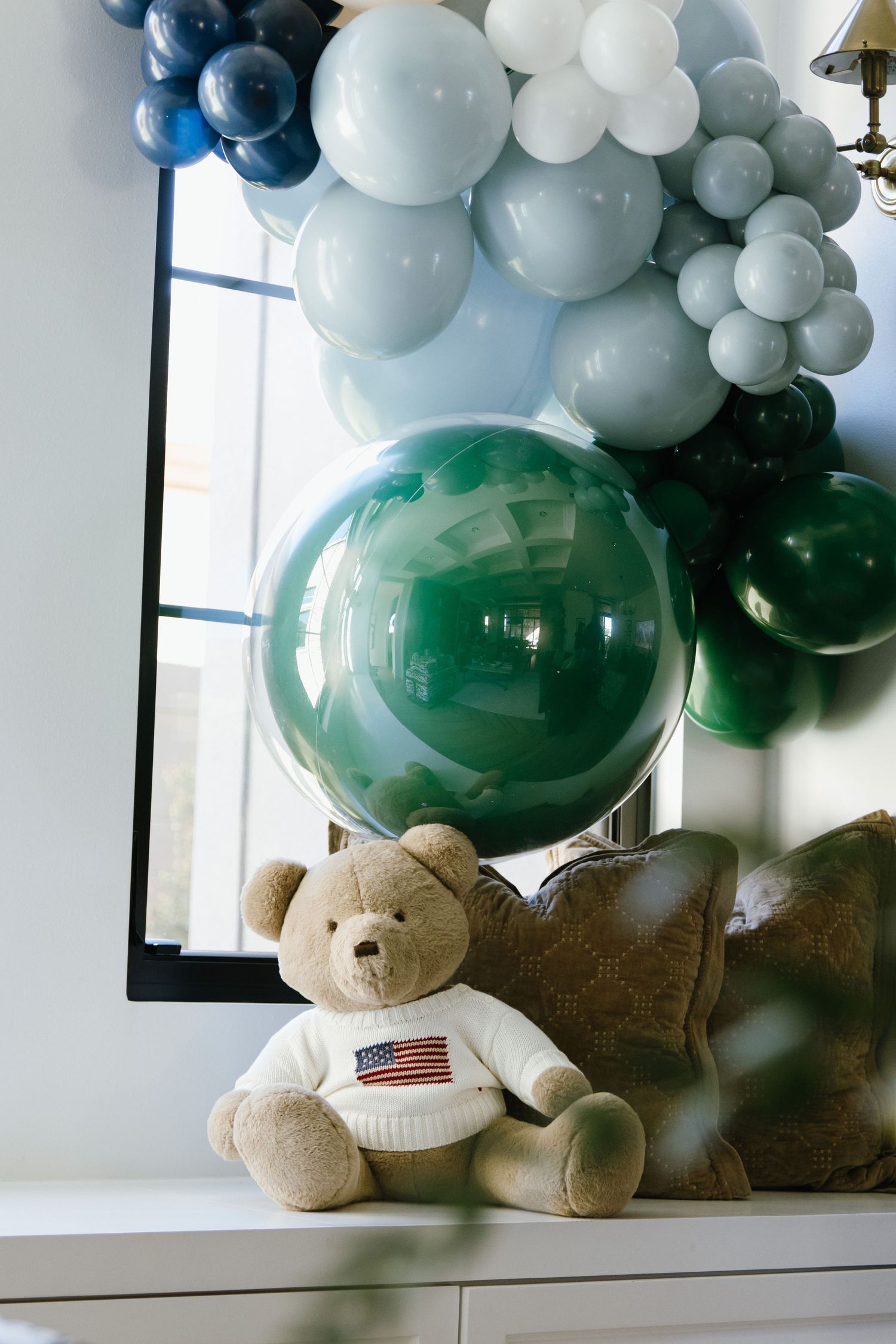 Balloon arch installation featuring green, blue, and white balloons with decorative teddy bears.