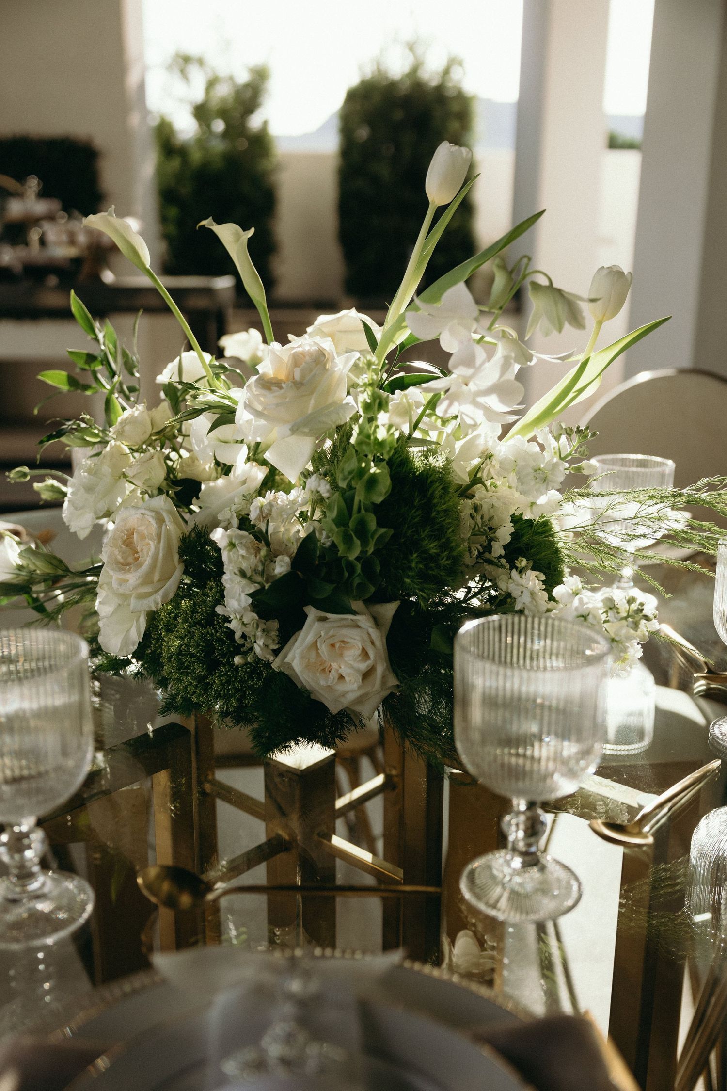 Elegant white floral centerpieces with roses and lilies in glass vases on dining tables.