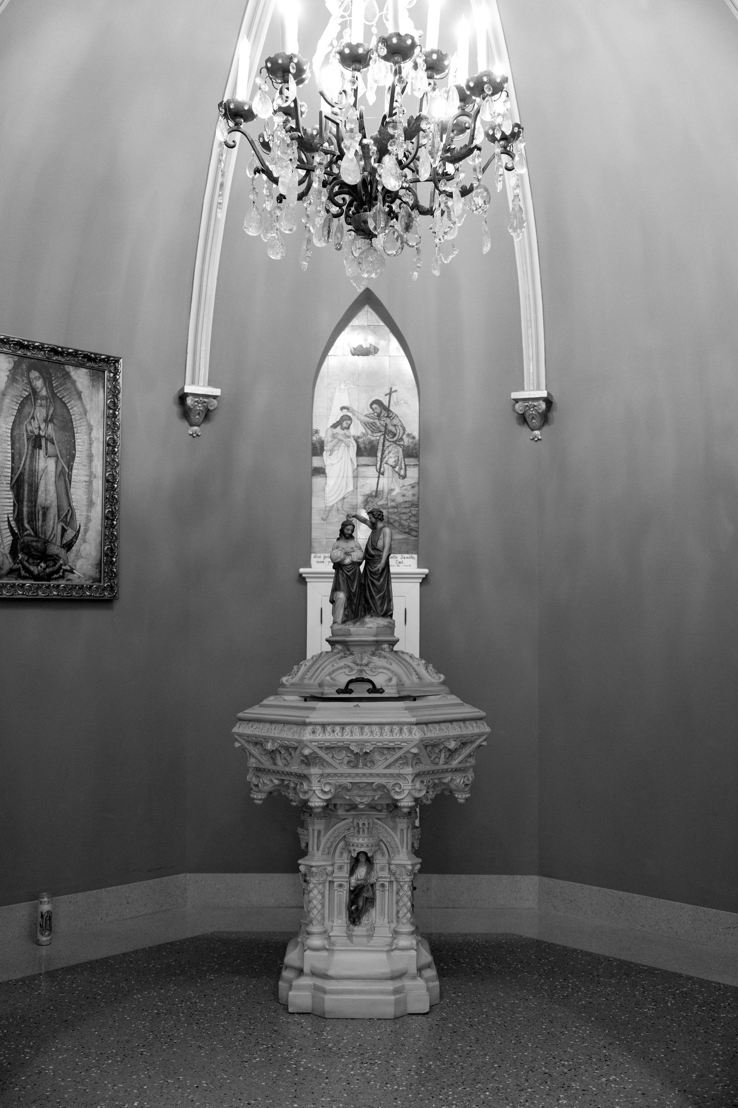 Ornate white altar with religious statues and chandelier in church setting.