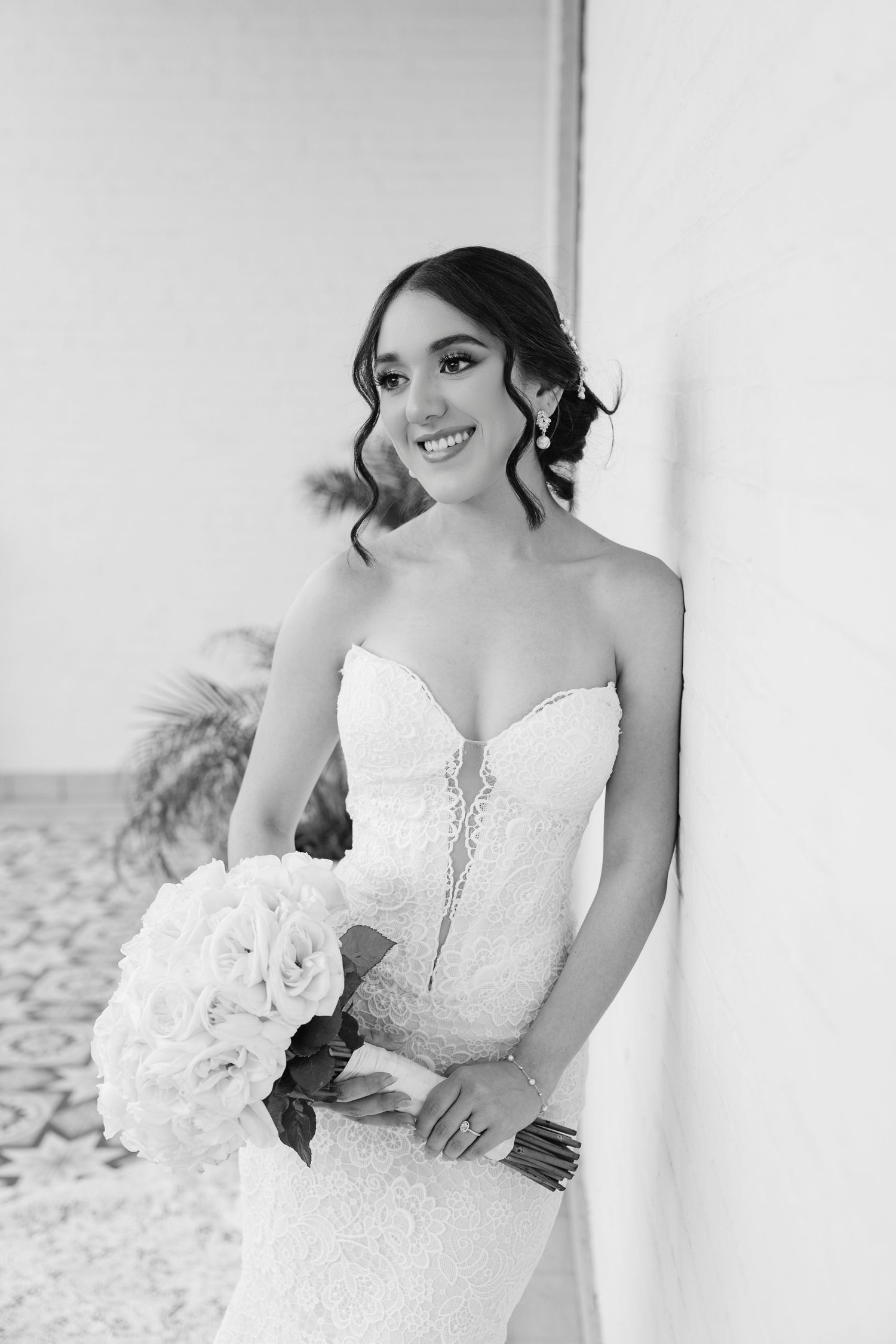 Bride in a white strapless wedding dress poses with a bouquet of white flowers in an elegant black and white portrait.
