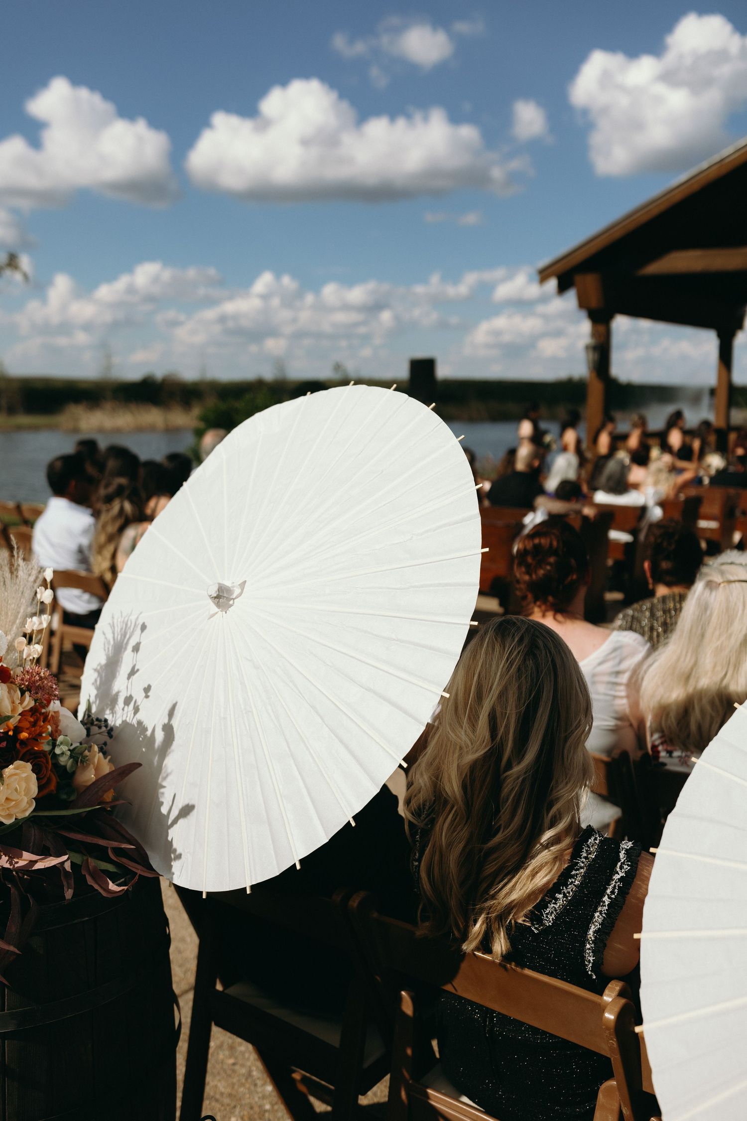 Wedding guests holding white paper parasols during outdoor ceremony.