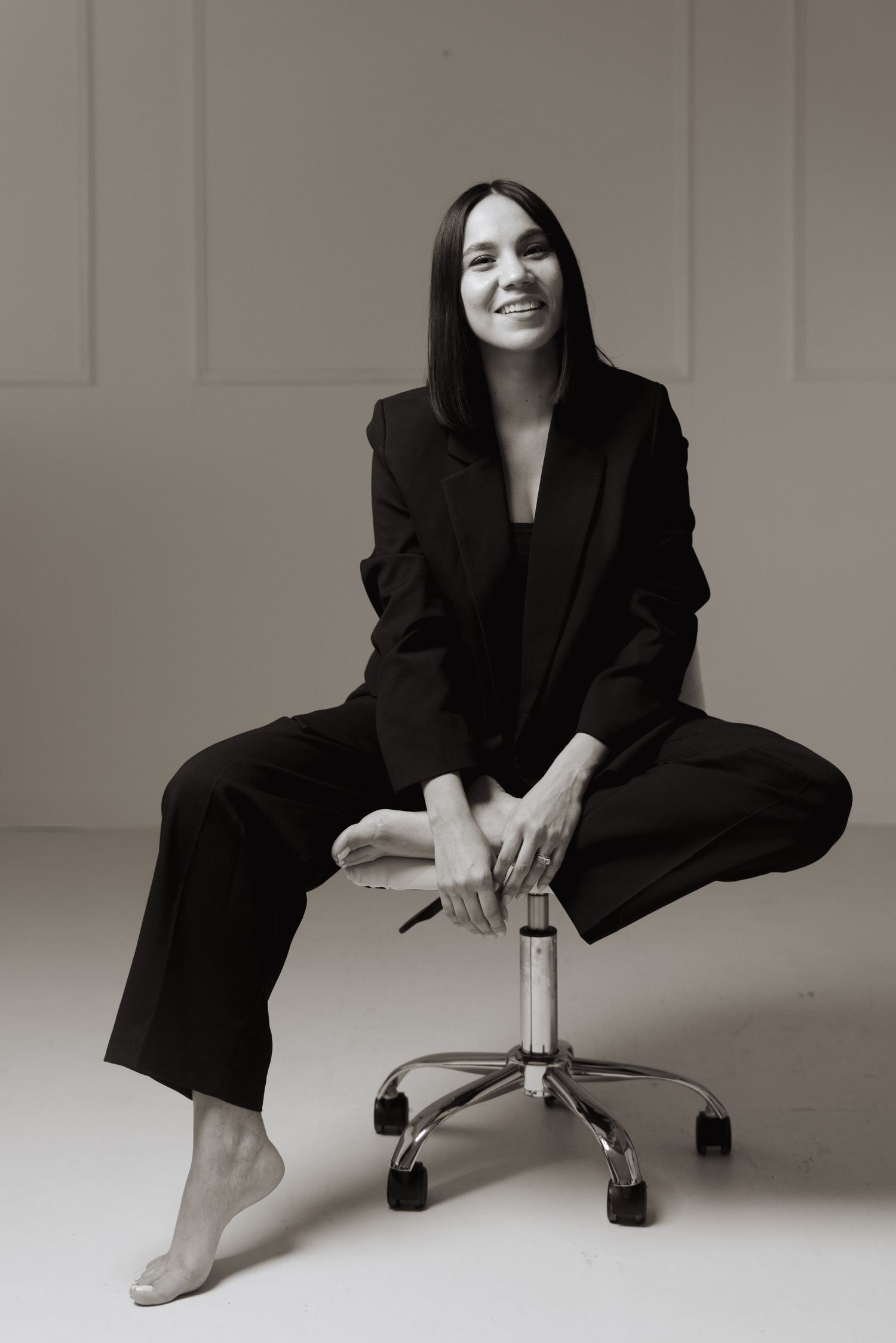 Artistic black and white portraits of photographer in relaxed poses on studio chair.