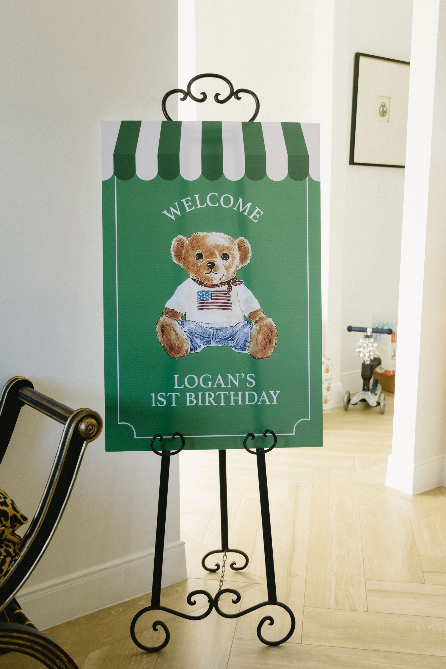 Green welcome sign with teddy bear design mounted on decorative metal easel.