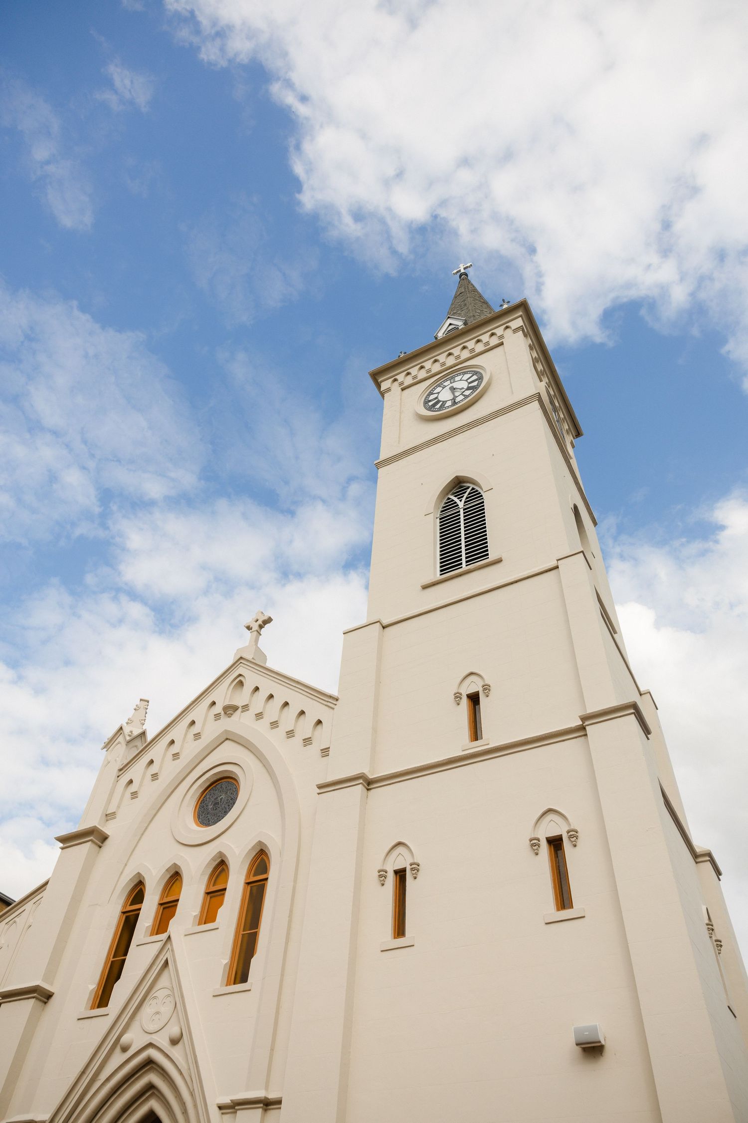 Tall white church steeple with clock tower against blue sky with fluffy clouds.