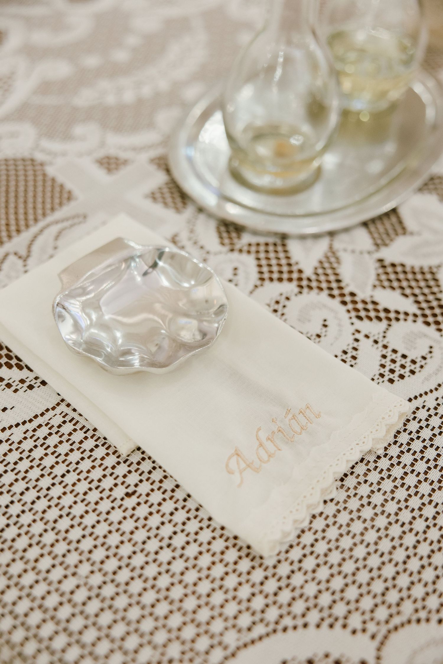 Wedding place cards arranged on intricate lace tablecloth with wine glasses.