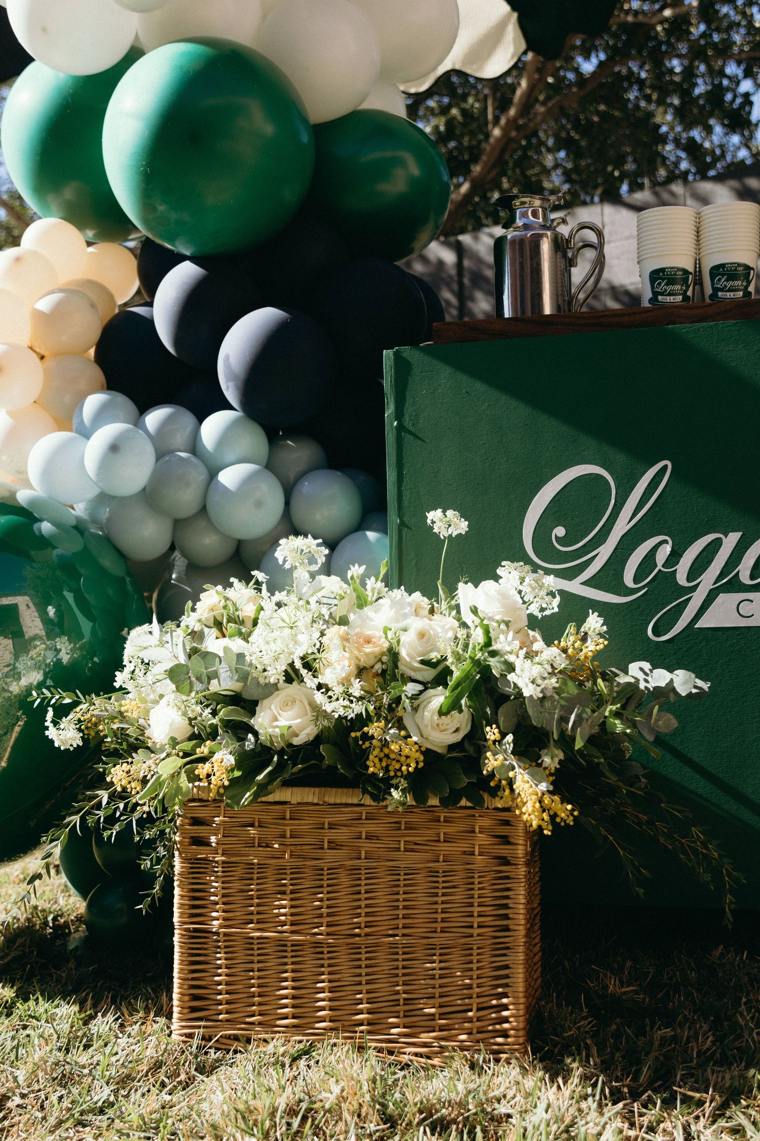 Elegant floral arrangements in wicker baskets with green and white balloon decorations.
