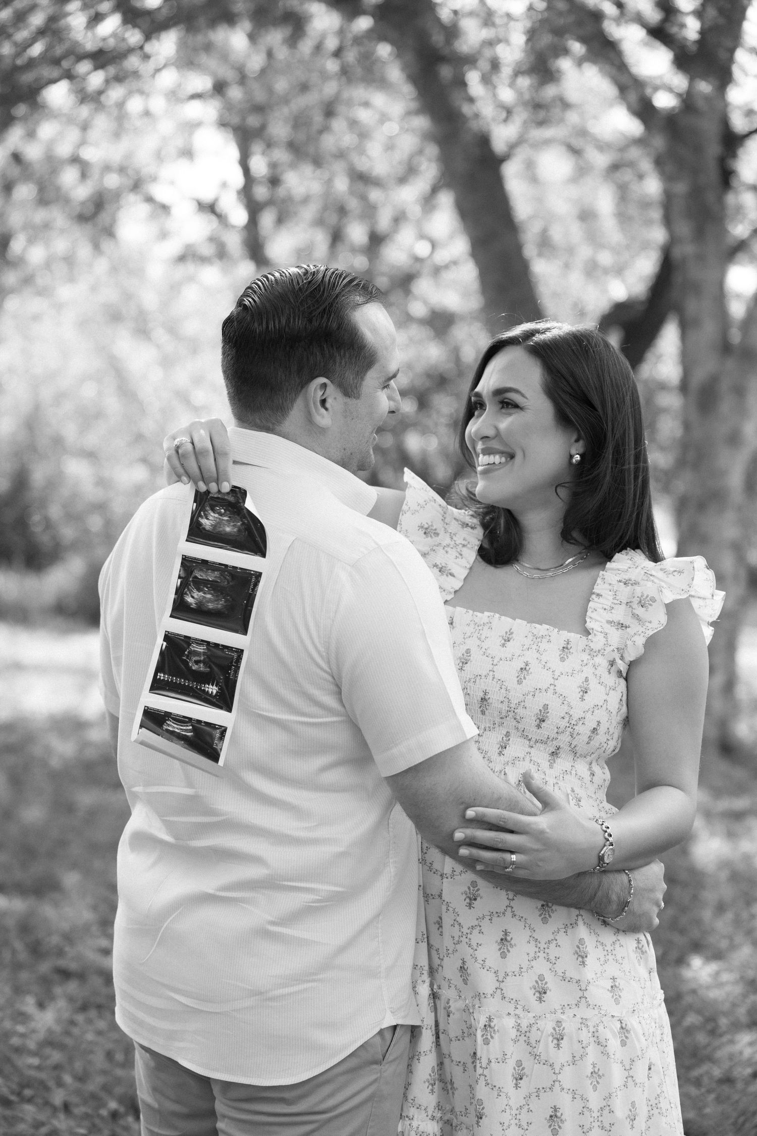 A couple shares a joyful moment while holding ultrasound photos in a romantic outdoor setting.