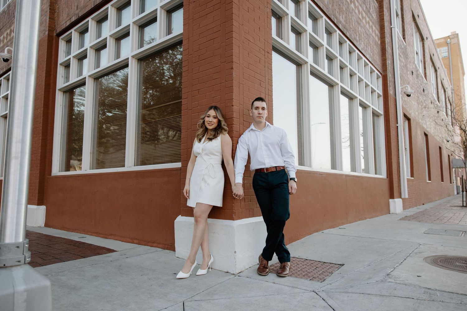 Couple walking together along a brick building exterior in matching white outfits.