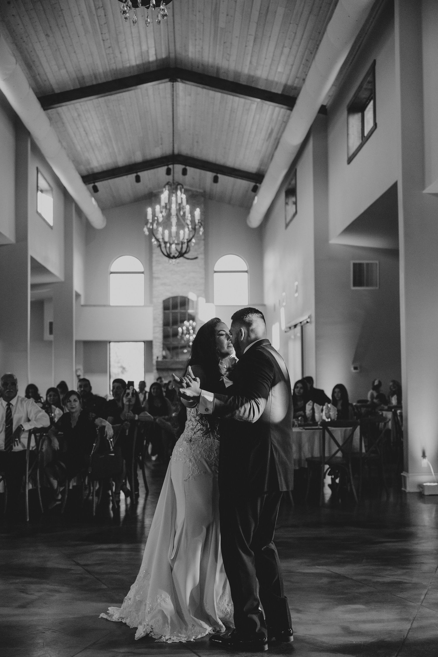 A couple shares their first dance in a grand ballroom with high ceilings and chandeliers.