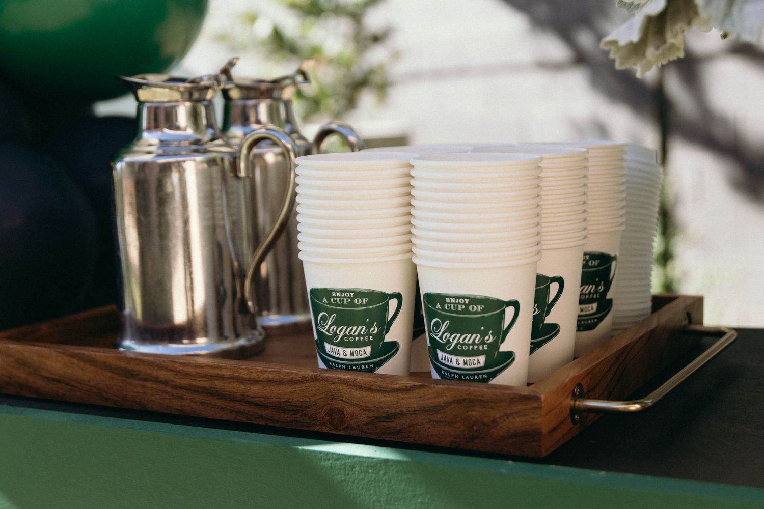 Wooden serving tray with coffee cups and metal containers for a party setup.