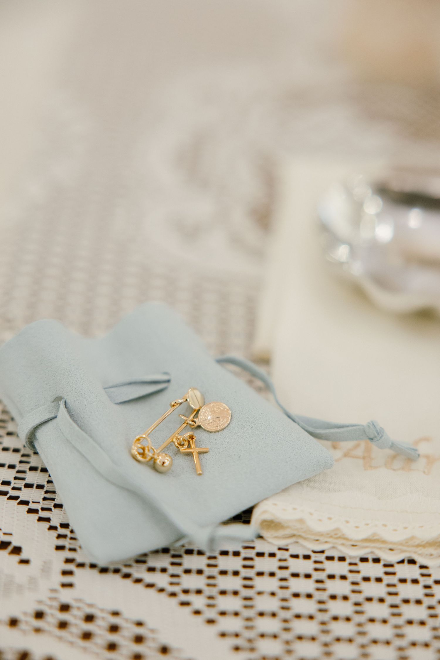 Light blue favor bags with gold jewelry accessories displayed on lace tablecloth.