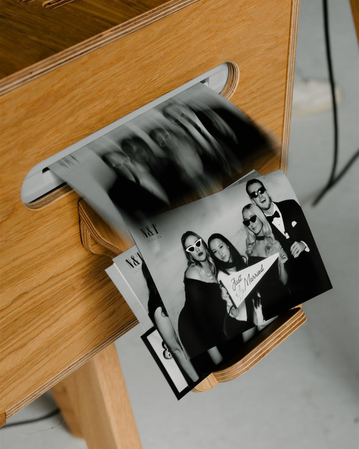 Black and white photo booth prints spilling from a wooden drawer, featuring elegantly dressed guests posing together.