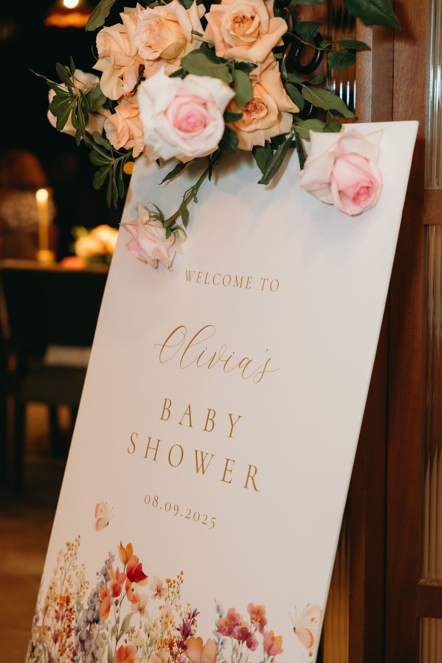 Baby shower welcome sign decorated with peach and pink roses and gold lettering.