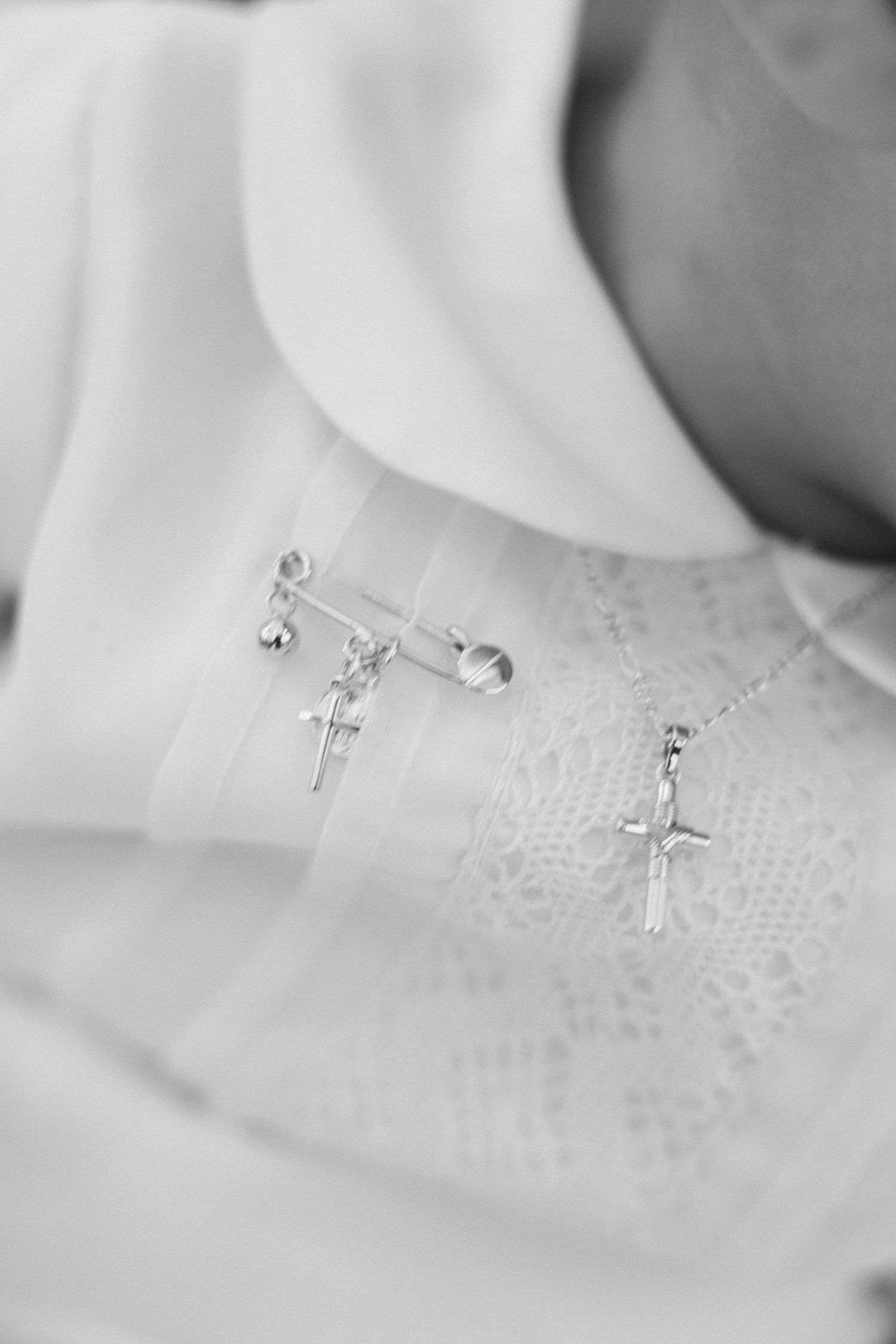 Detailed black and white photo of silver cross pins on white christening gown fabric.