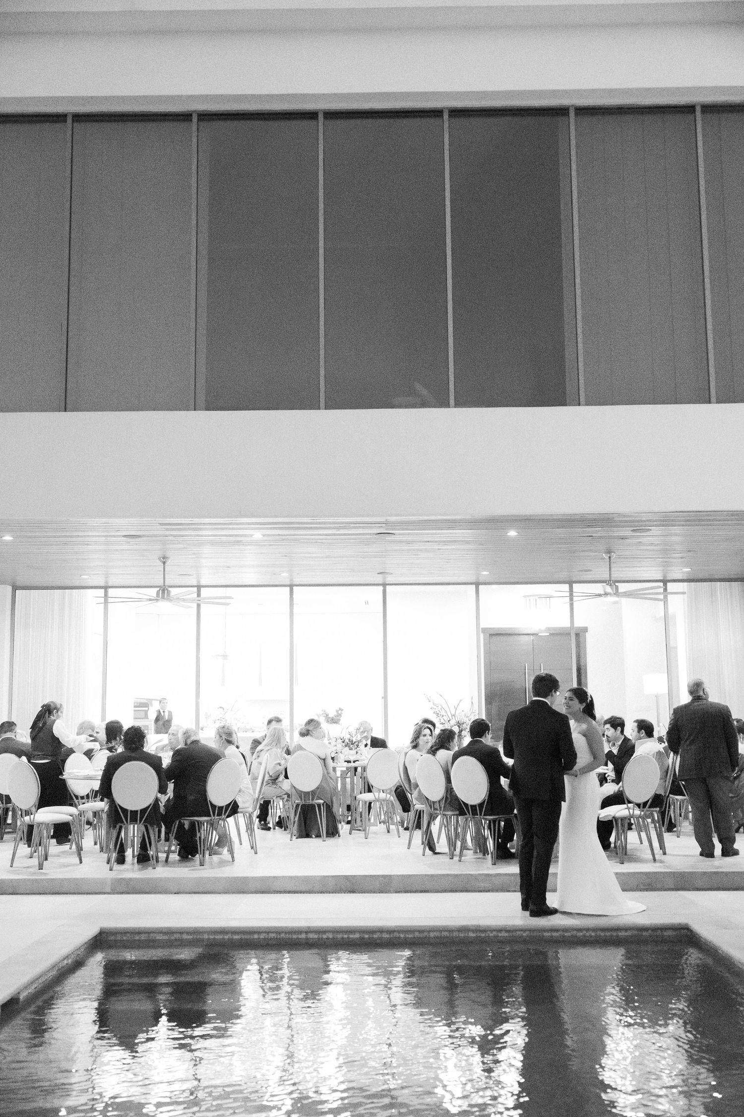 Black and white panoramic view of a modern indoor wedding reception venue with guests seated at tables.