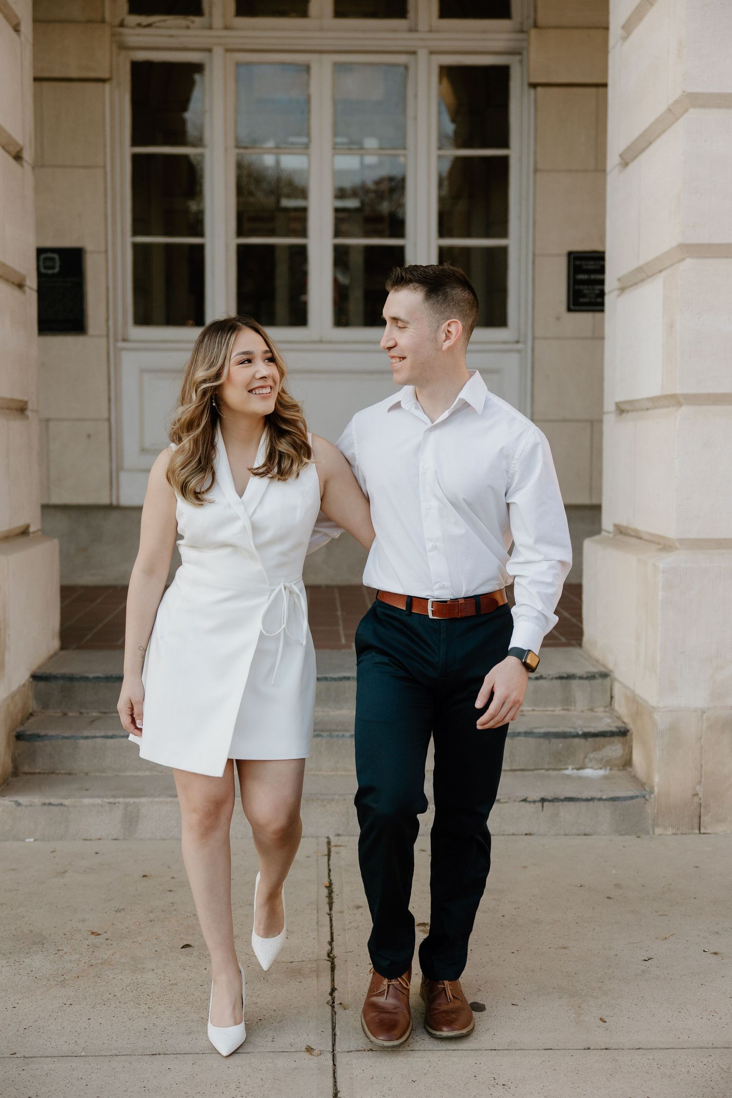 Couple in white sitting and laughing together on concrete steps of a building.
