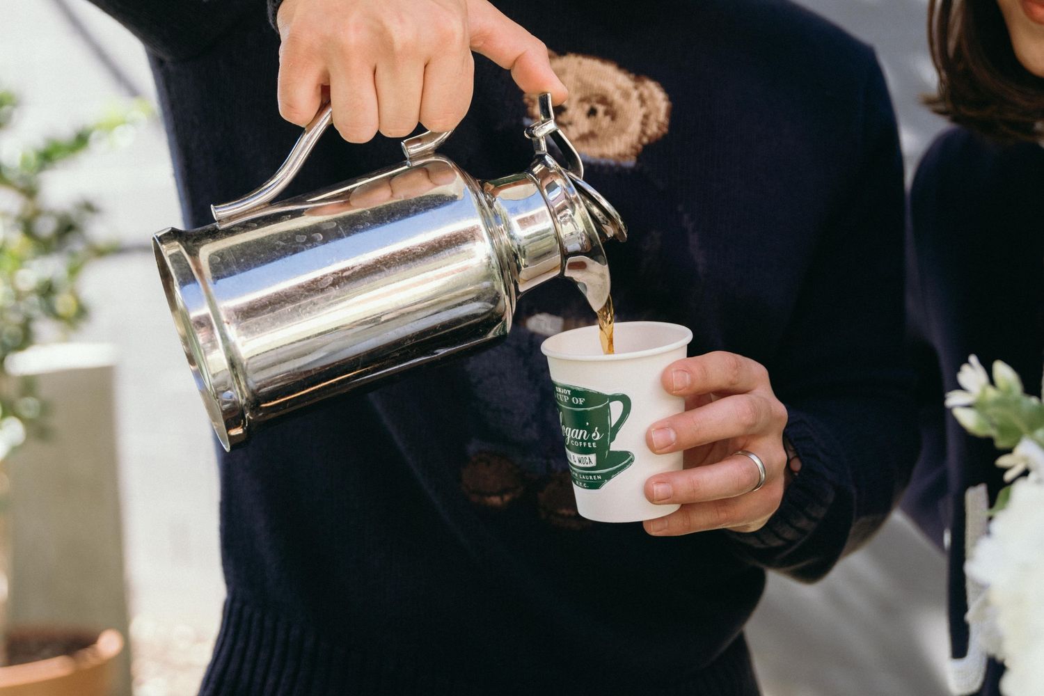 Coffee being poured from a silver kettle into white ceramic cups.