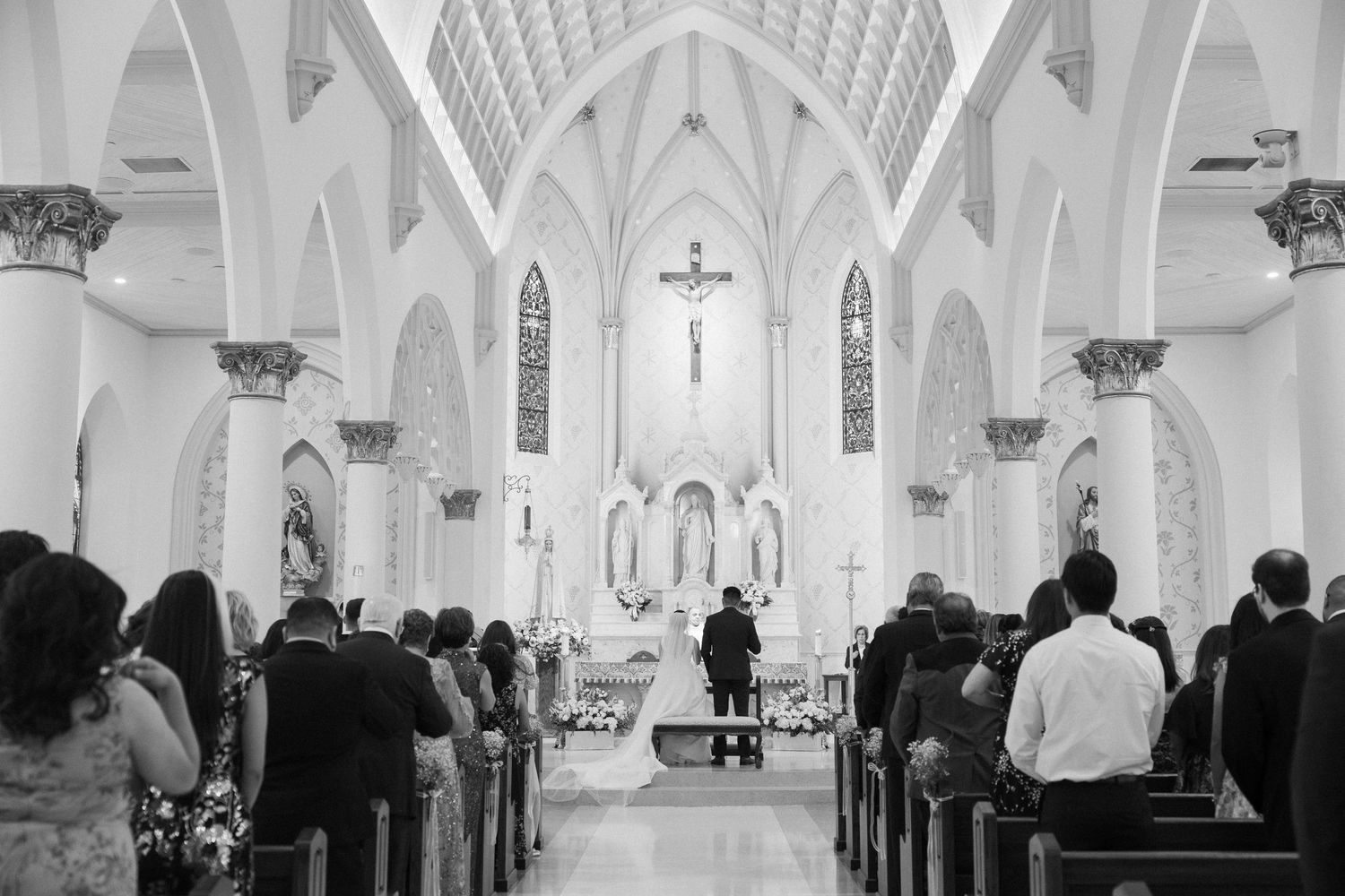 Black and white photo of a church interior with vaulted ceilings and stained glass windows.