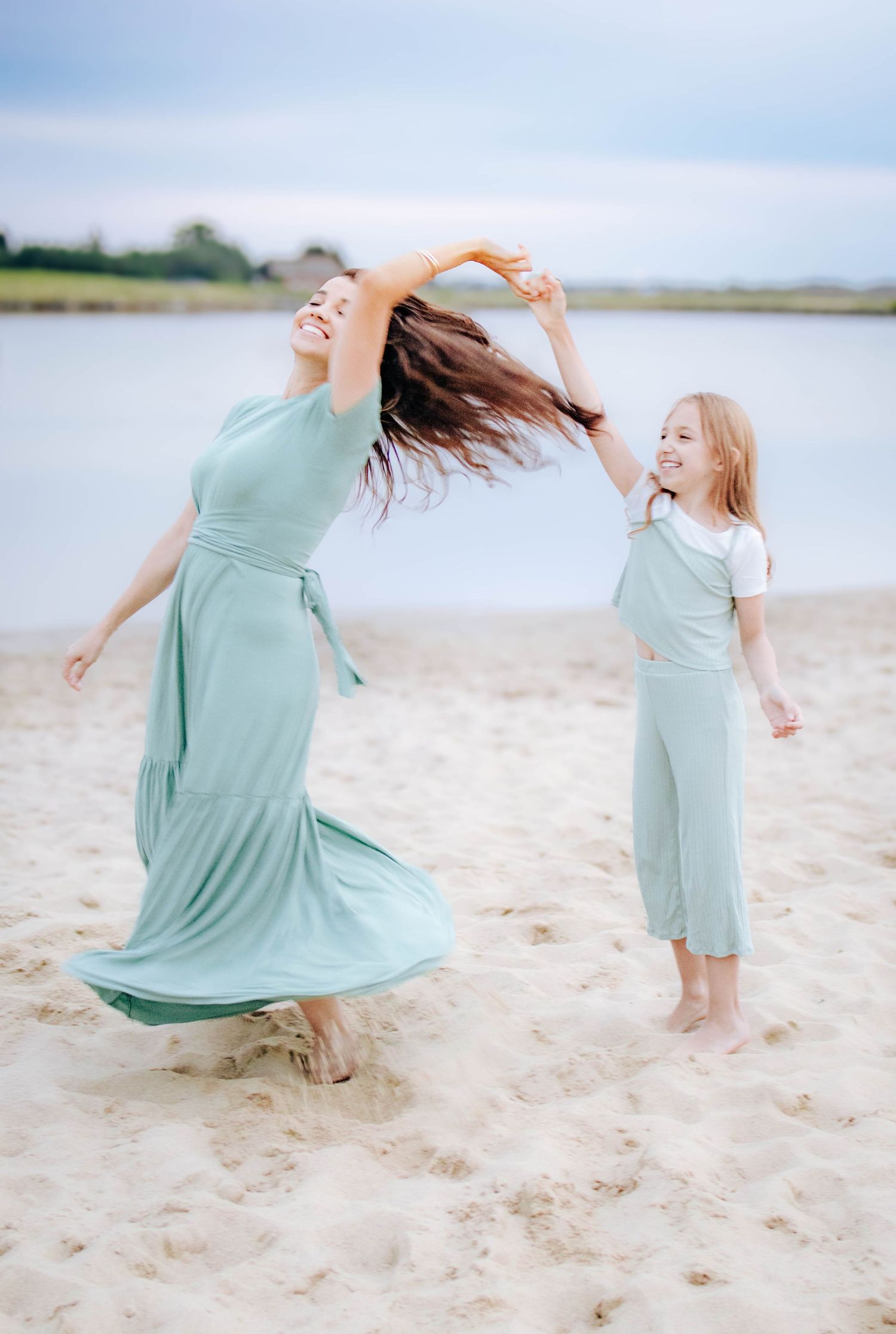 mother and daughter spinning together on sandy beach at sunset family photography