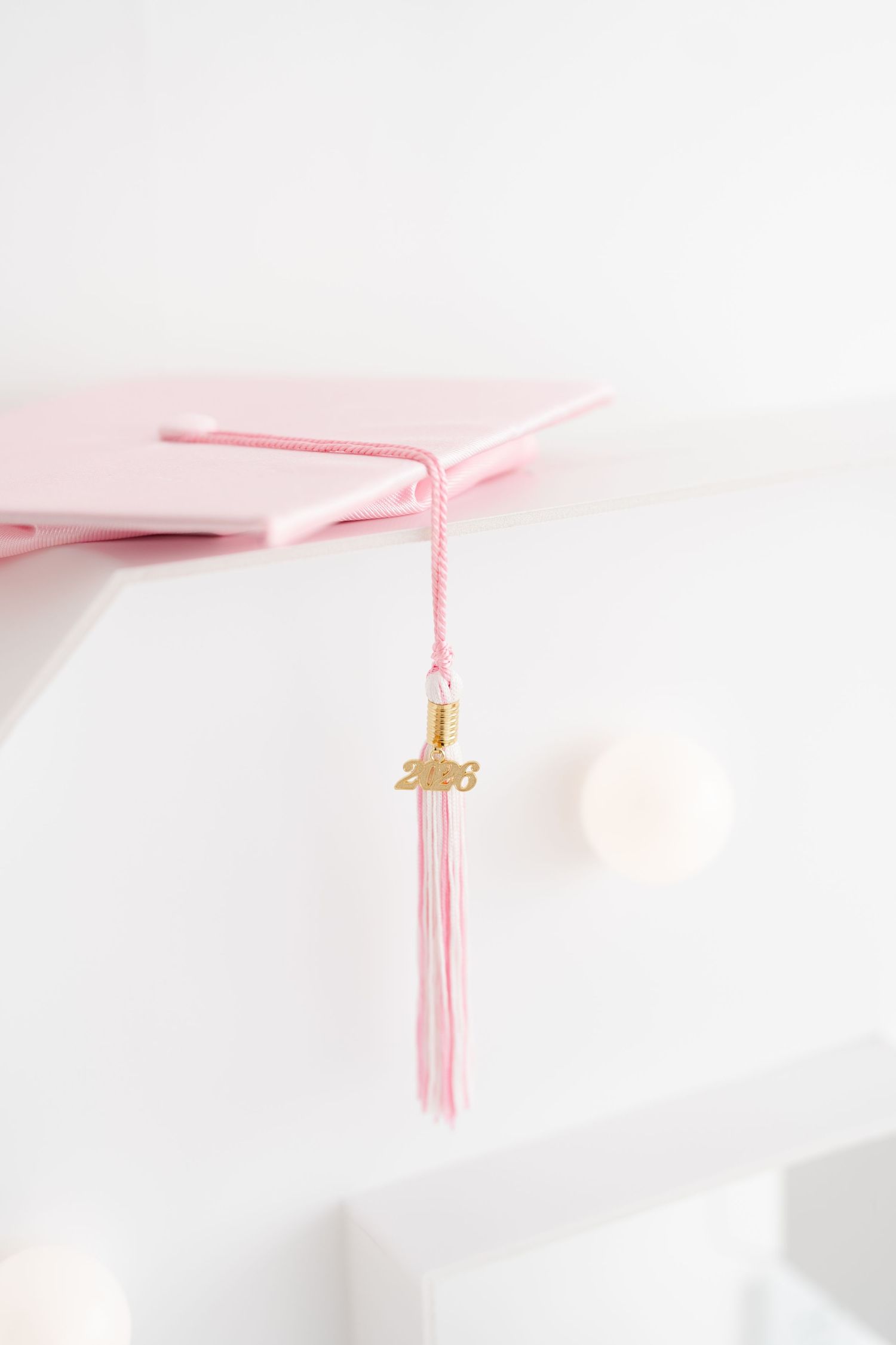 Pink graduation cap with tassel and gold 2026 charm displayed on white shelf.Preschool and Kindergarten Graduation Portraits in Clarksville