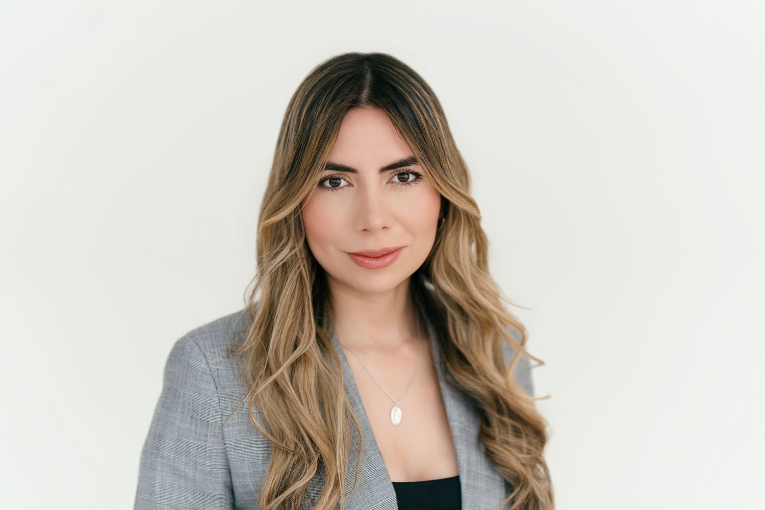 Professional headshot portrait of someone with long wavy blonde hair wearing a black blazer against a white background.