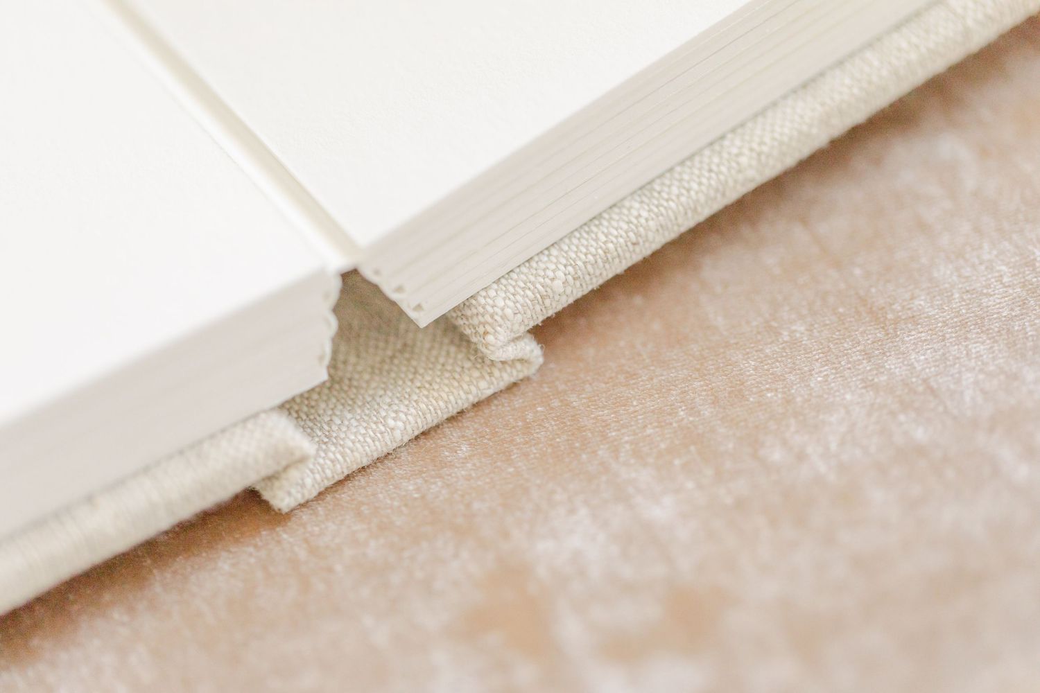 Close-up of a white hardcover book spine with linen binding detail on a beige textured surface.