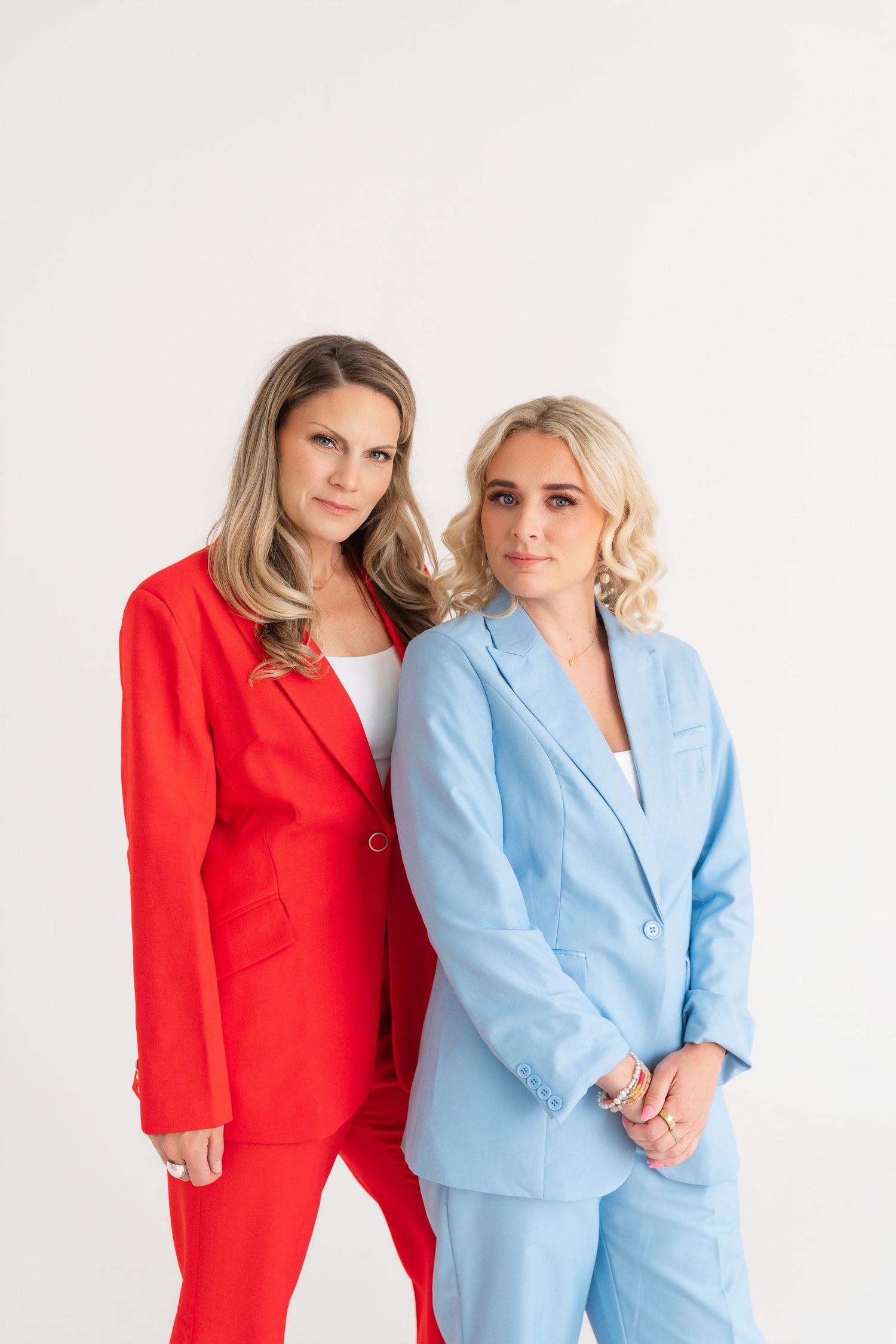 Two women in matching suits, one red and one blue, posing together against a white background.