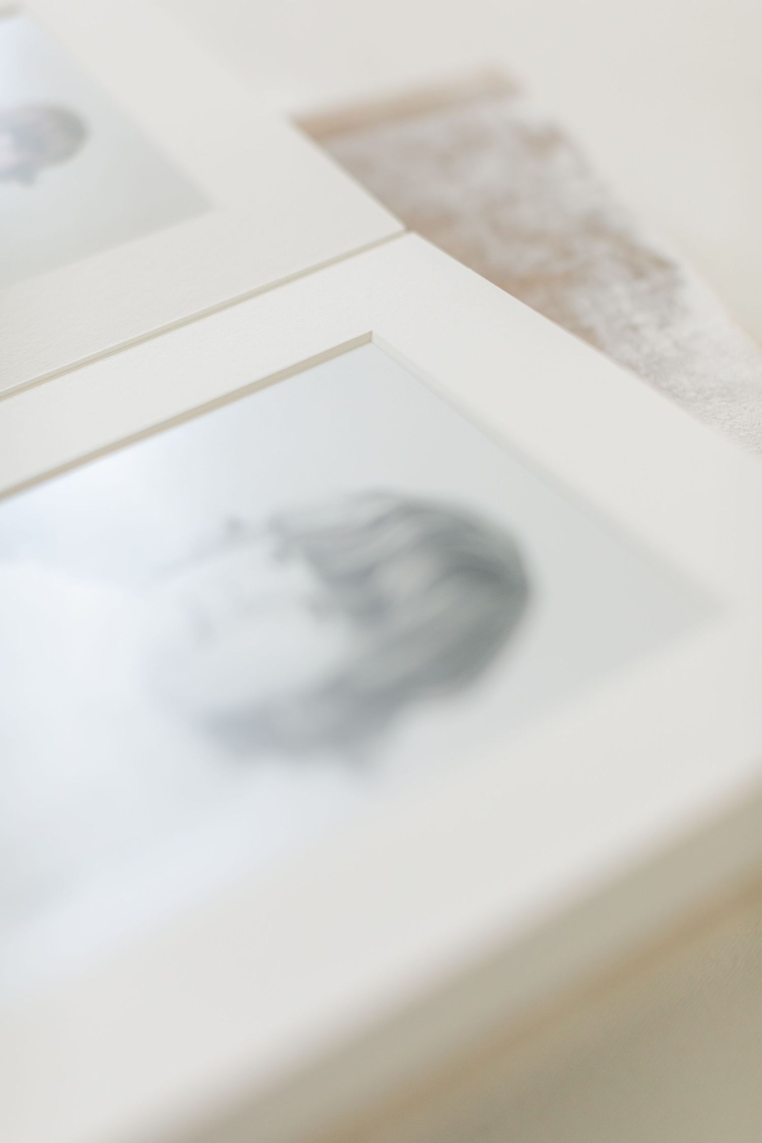 Two white picture frames displaying soft, blurred artwork in muted tones arranged on a light surface.