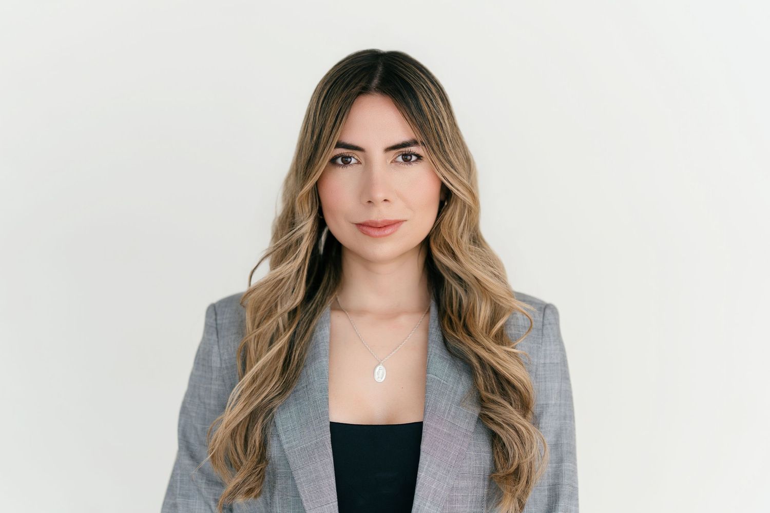Professional headshot of someone in a gray blazer and black top with long wavy hair against a light background.