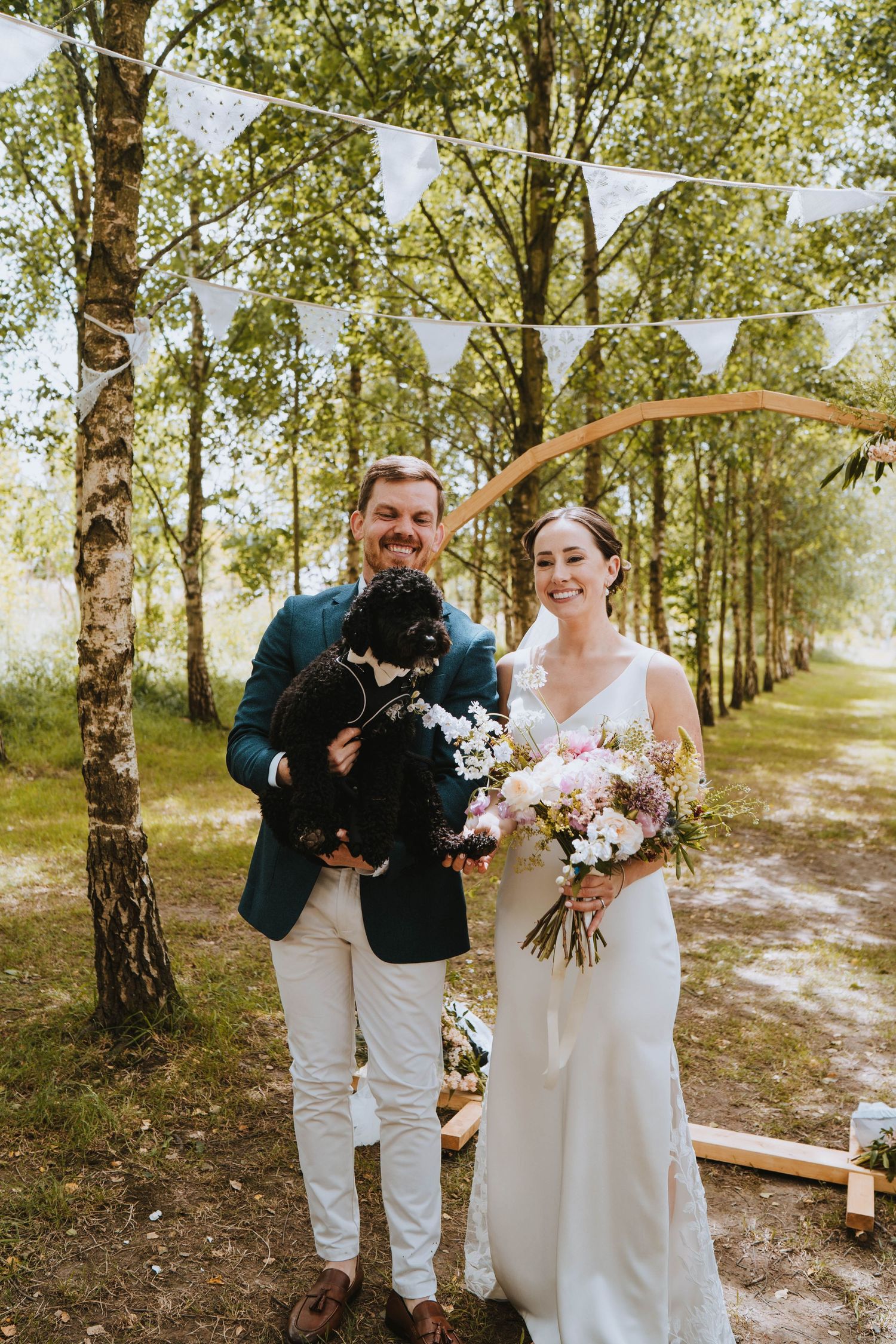 Bride and groom with dog smiling in forest aisle Devon wedding by Capture You Photography