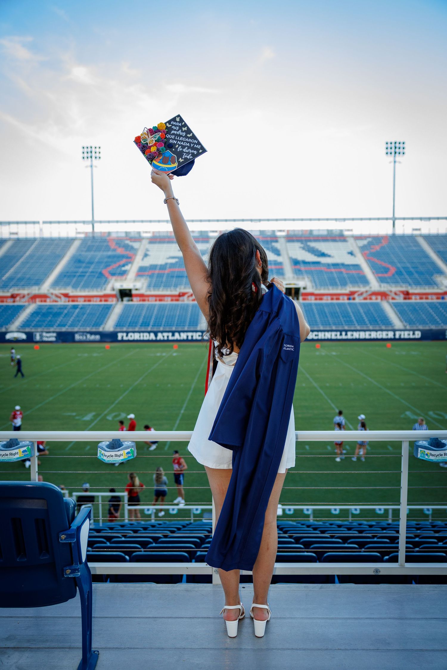 FAU graduate holding up graduation cap in front of stadium.