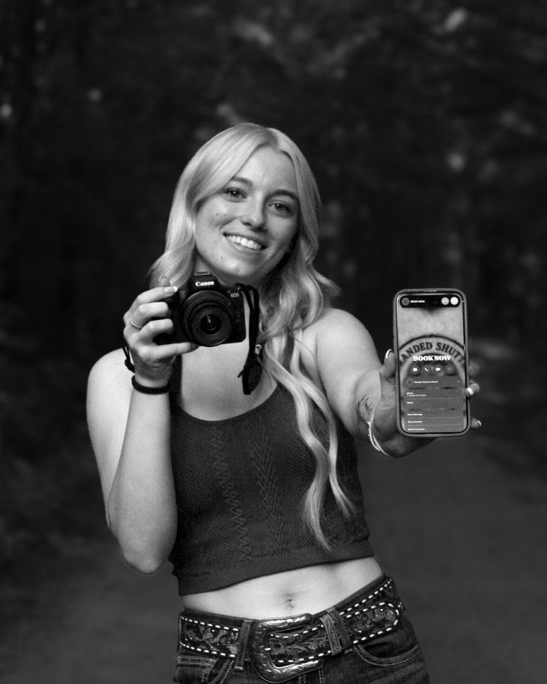 A photographer holds both a camera and smartphone while taking pictures in the woods.