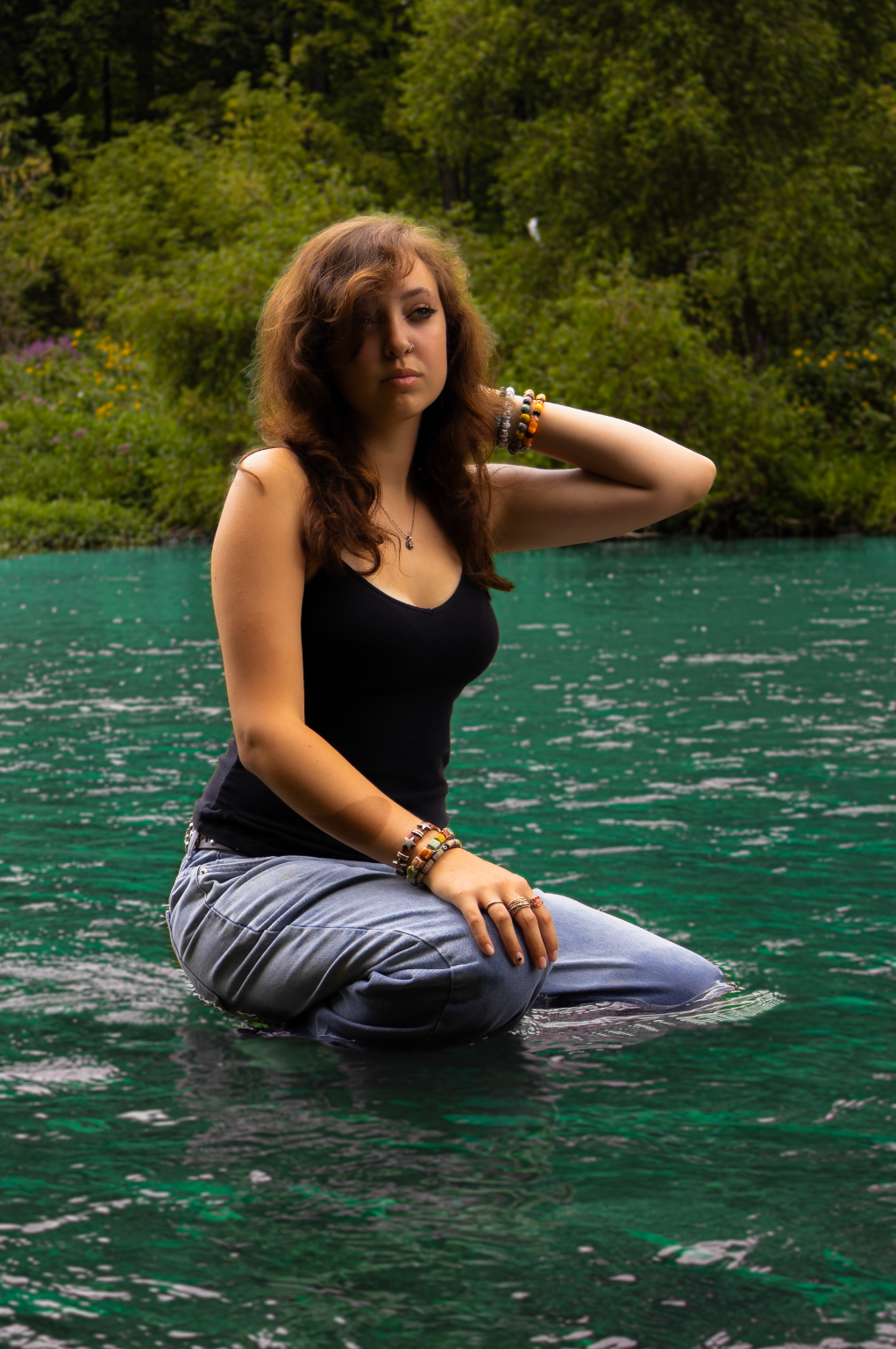 A person sits gracefully on a rock in a black tank top beside stunning turquoise waters surrounded by lush greenery.